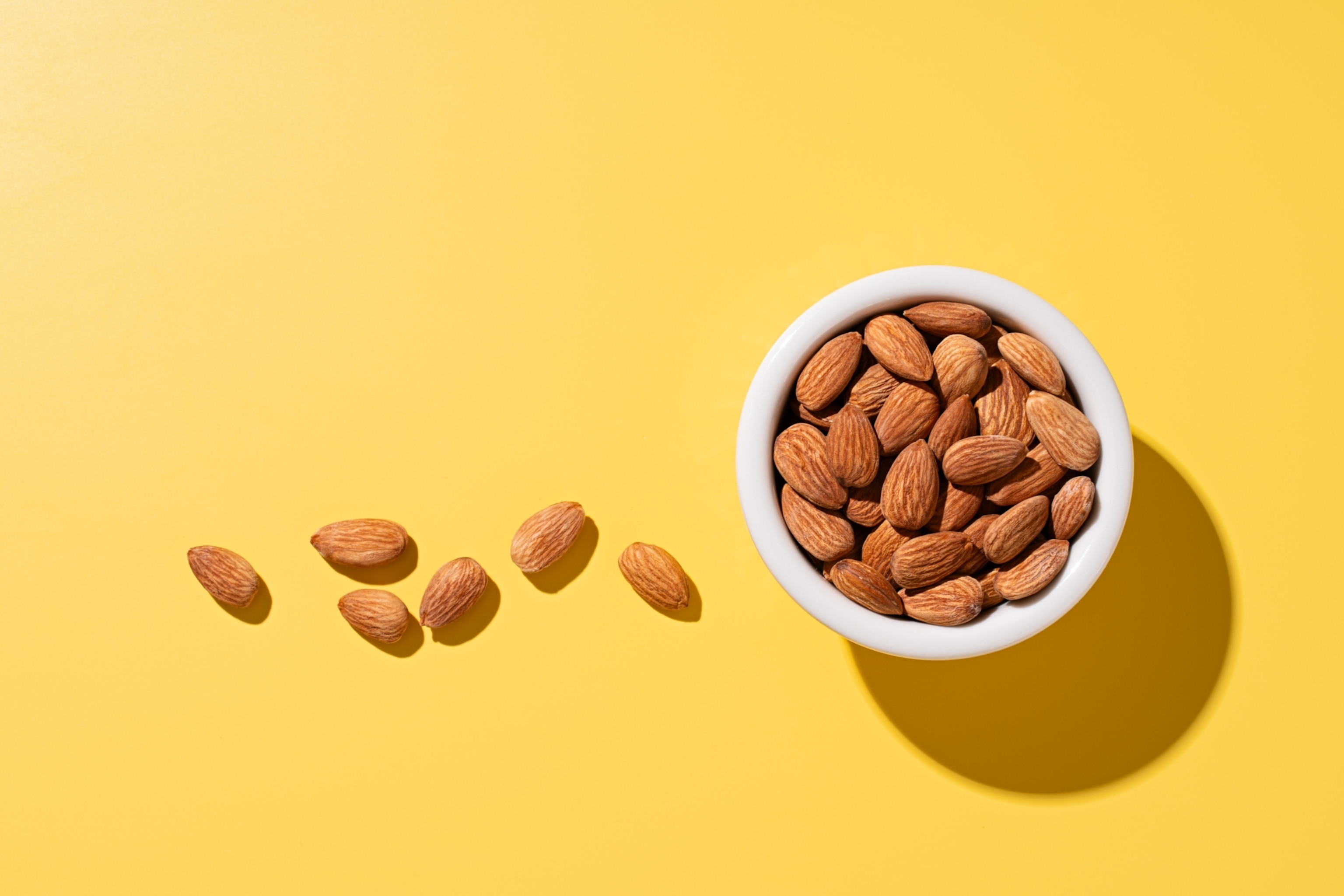 A bowl of almonds from above, on a yellow surface.