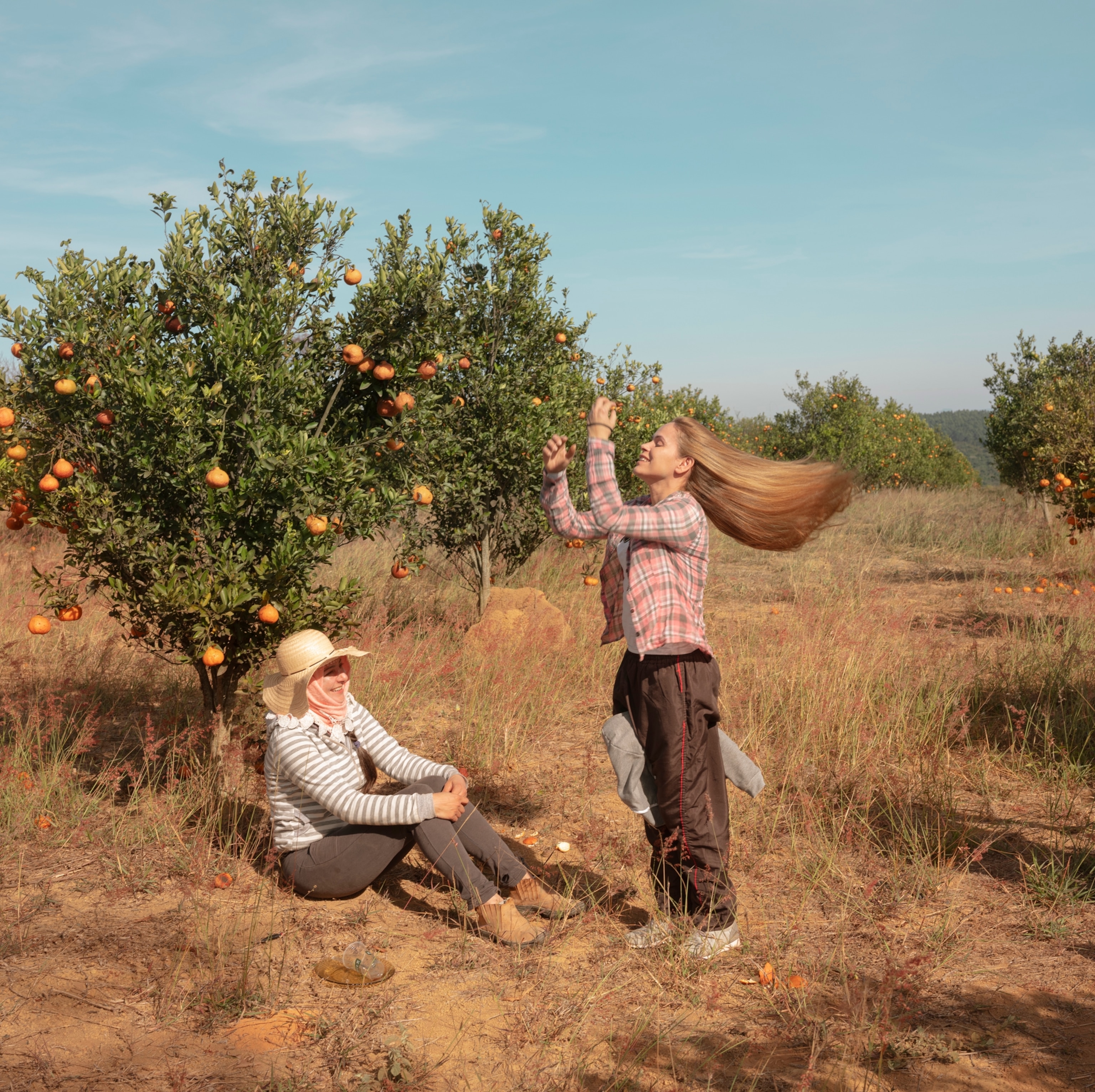 two women, one sitting and one standing, under an orange tree.