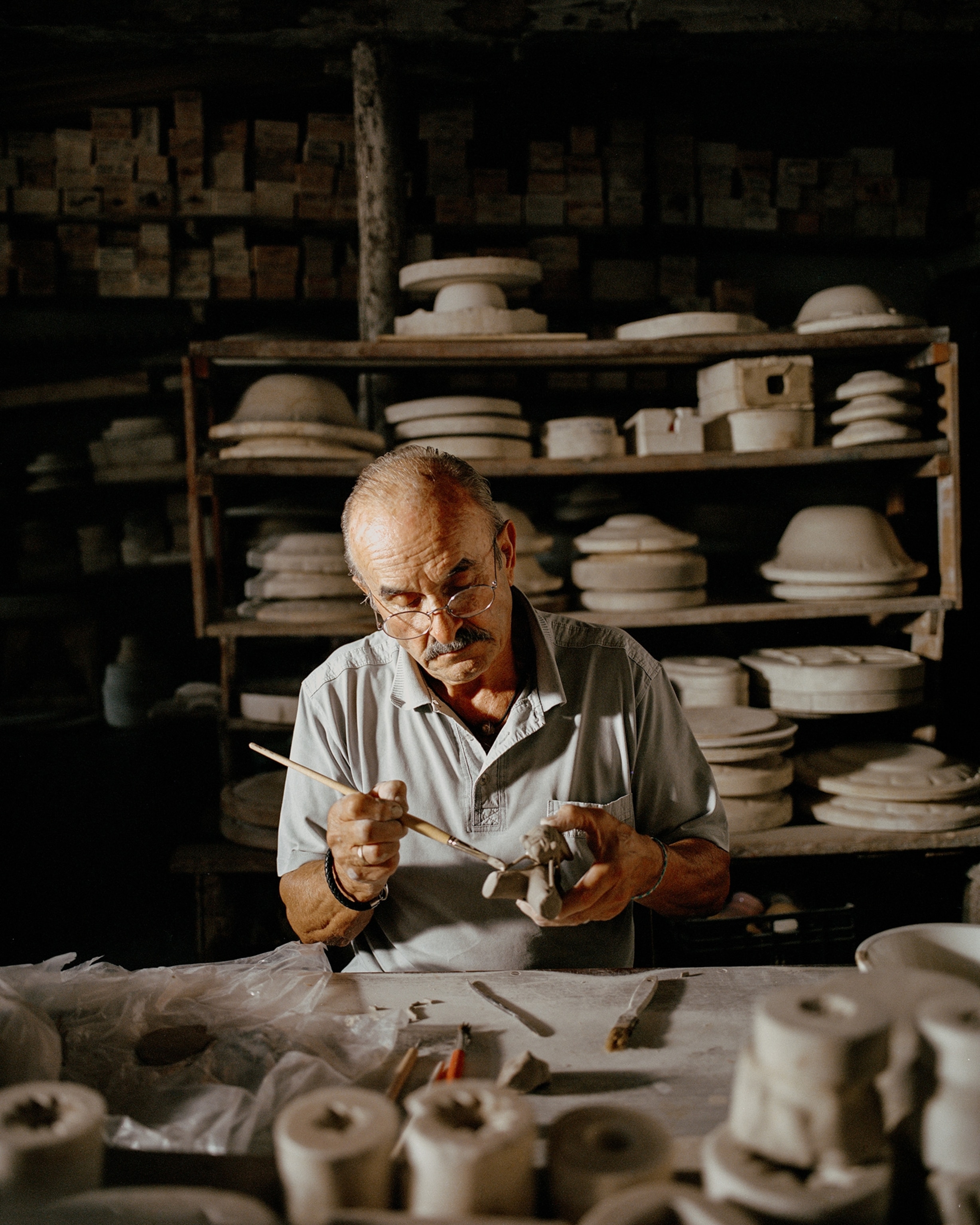 Bernard Amy uses a paint brush to wet clay so he can combine the cicada part, the base, and a few additional details like a leaf.