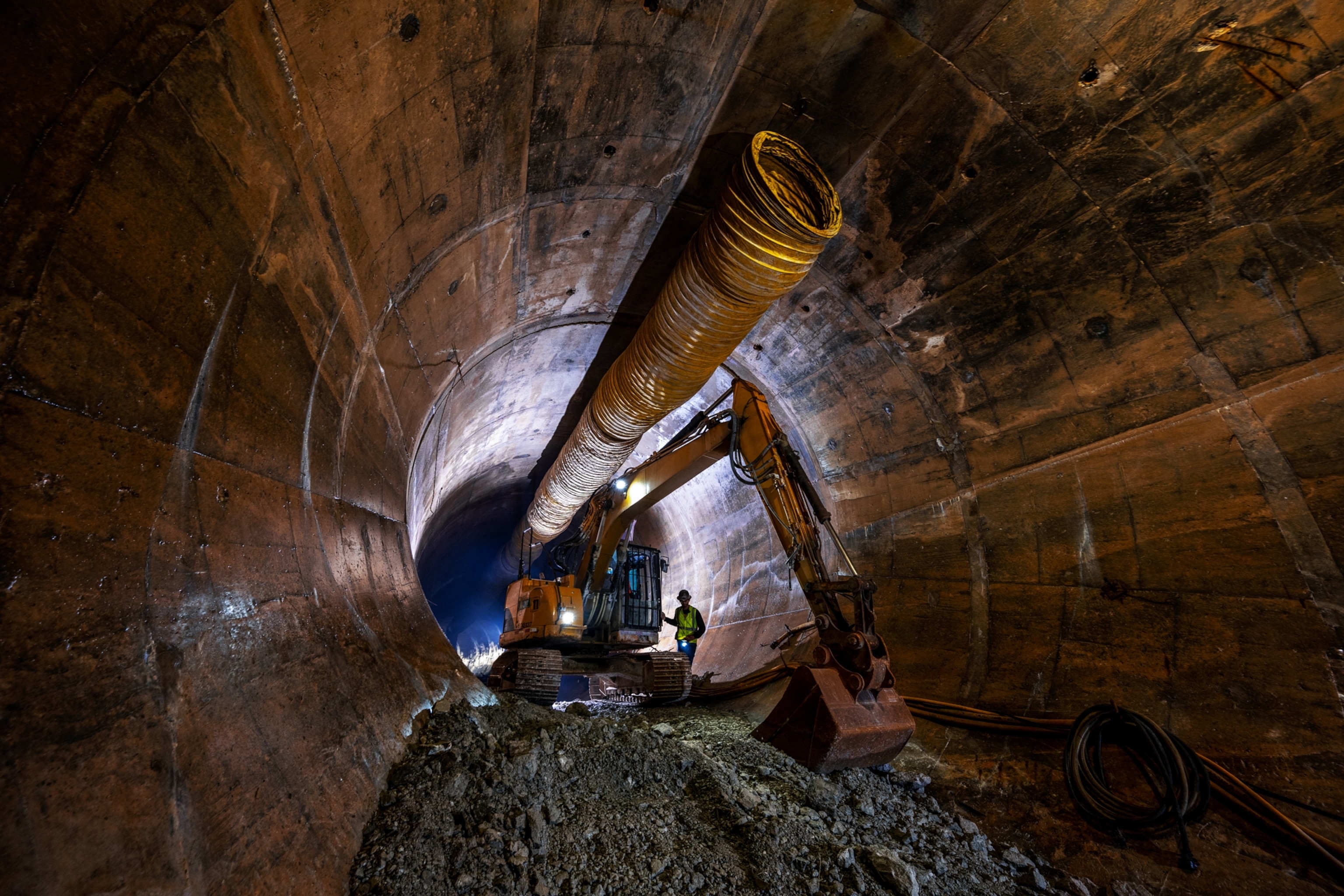 heavy machinery, pipes, and workers inside a tunnel.