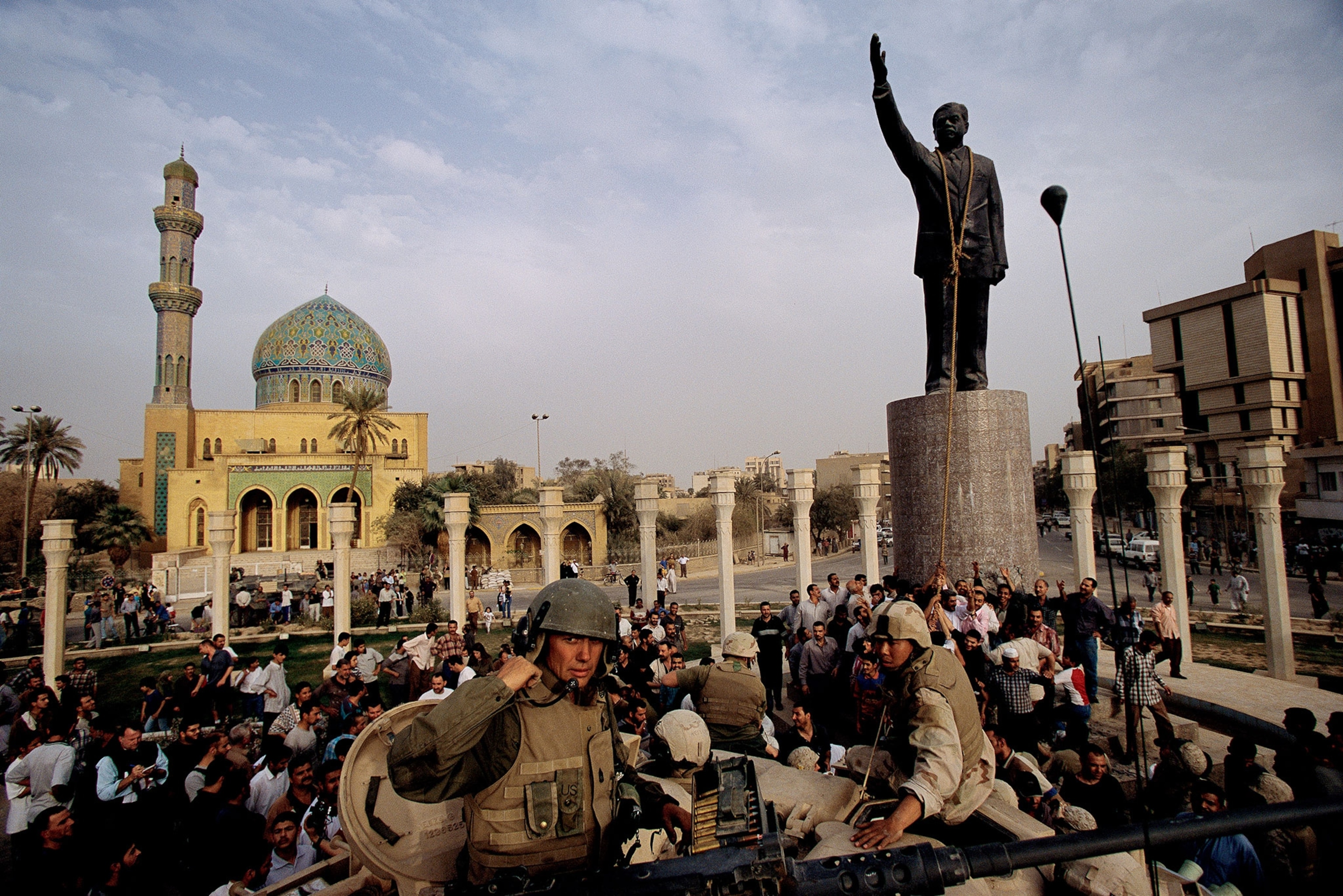 A large group of people and soldiers gathered in a square in Baghdad in front of a statute