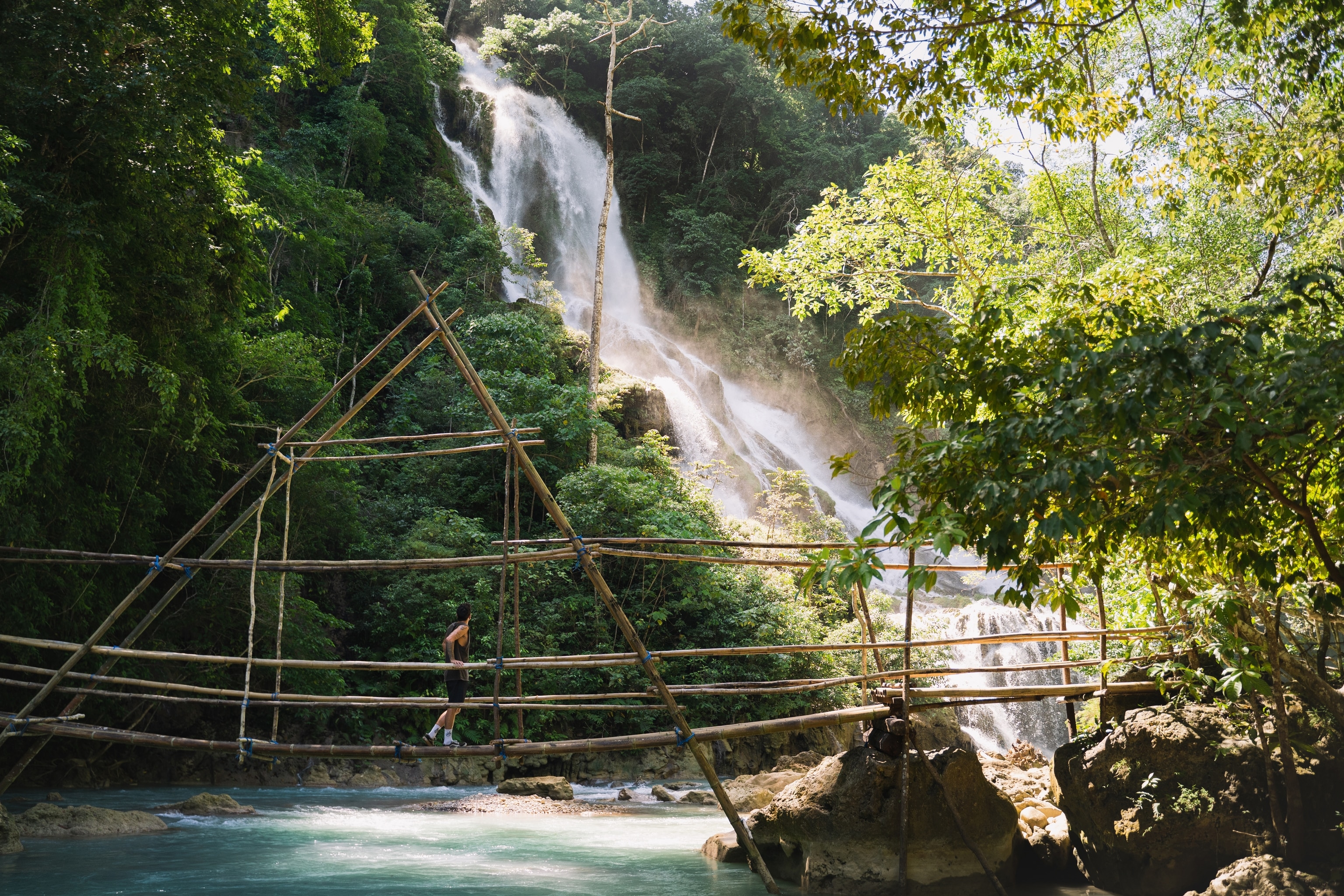 Man walking over jungle bridge with a waterfall in the background
