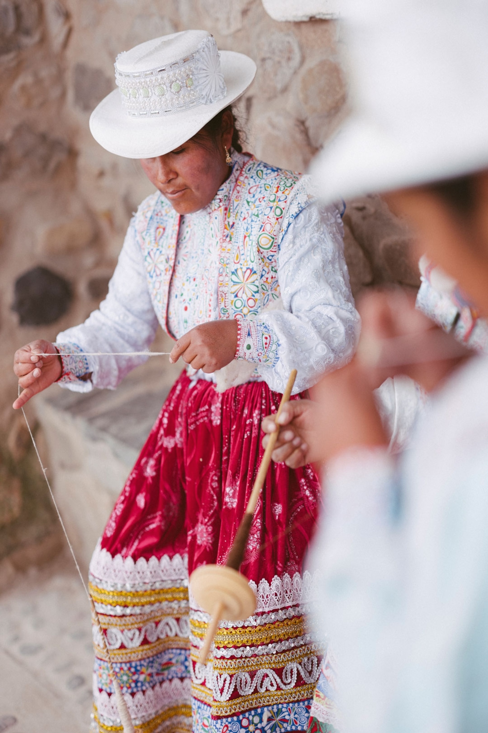 Woman wearing a hat and patterned garments weaves pieces of wool