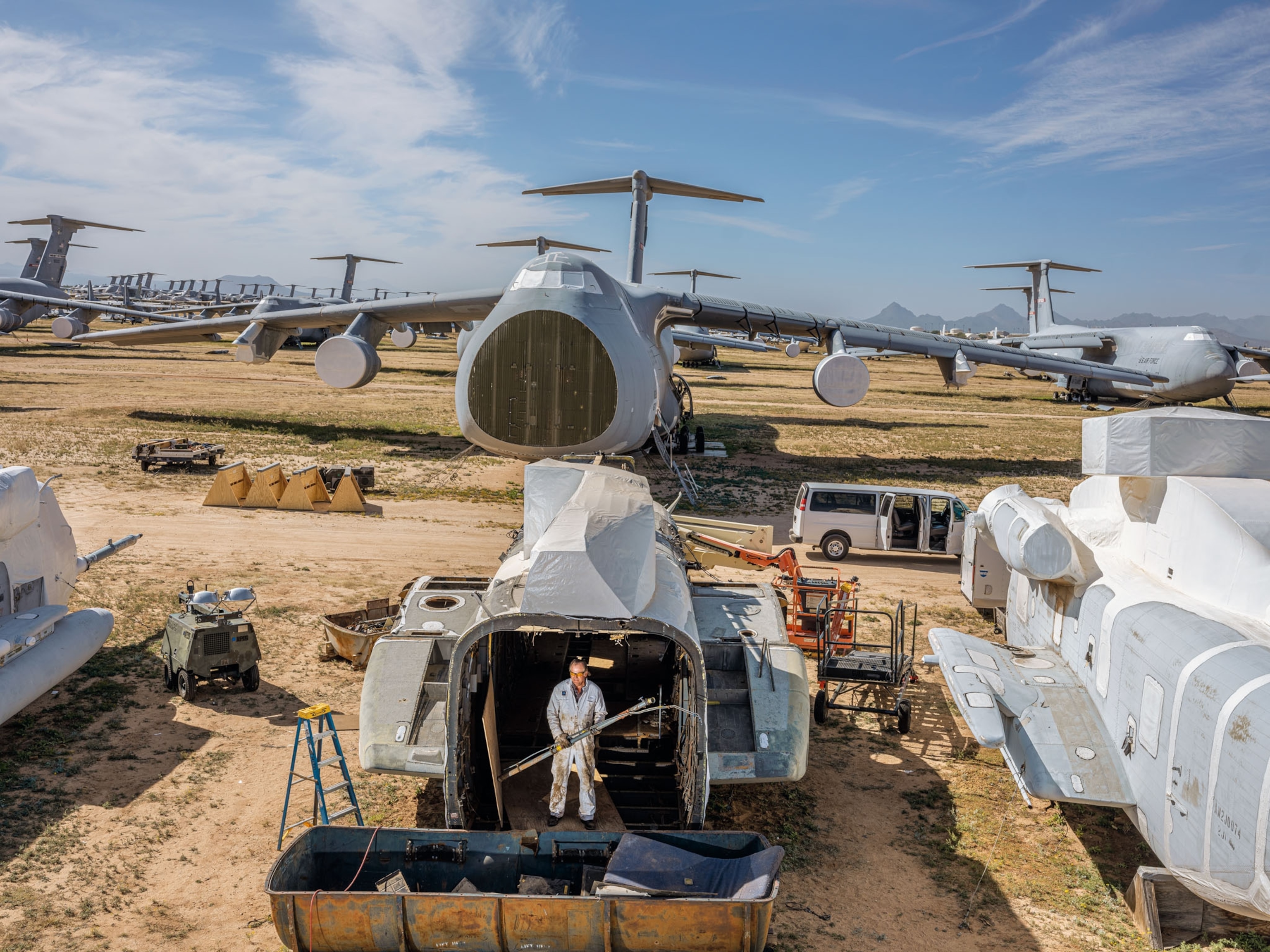a man in a white suit standing in a storage unit with airplanes in the background