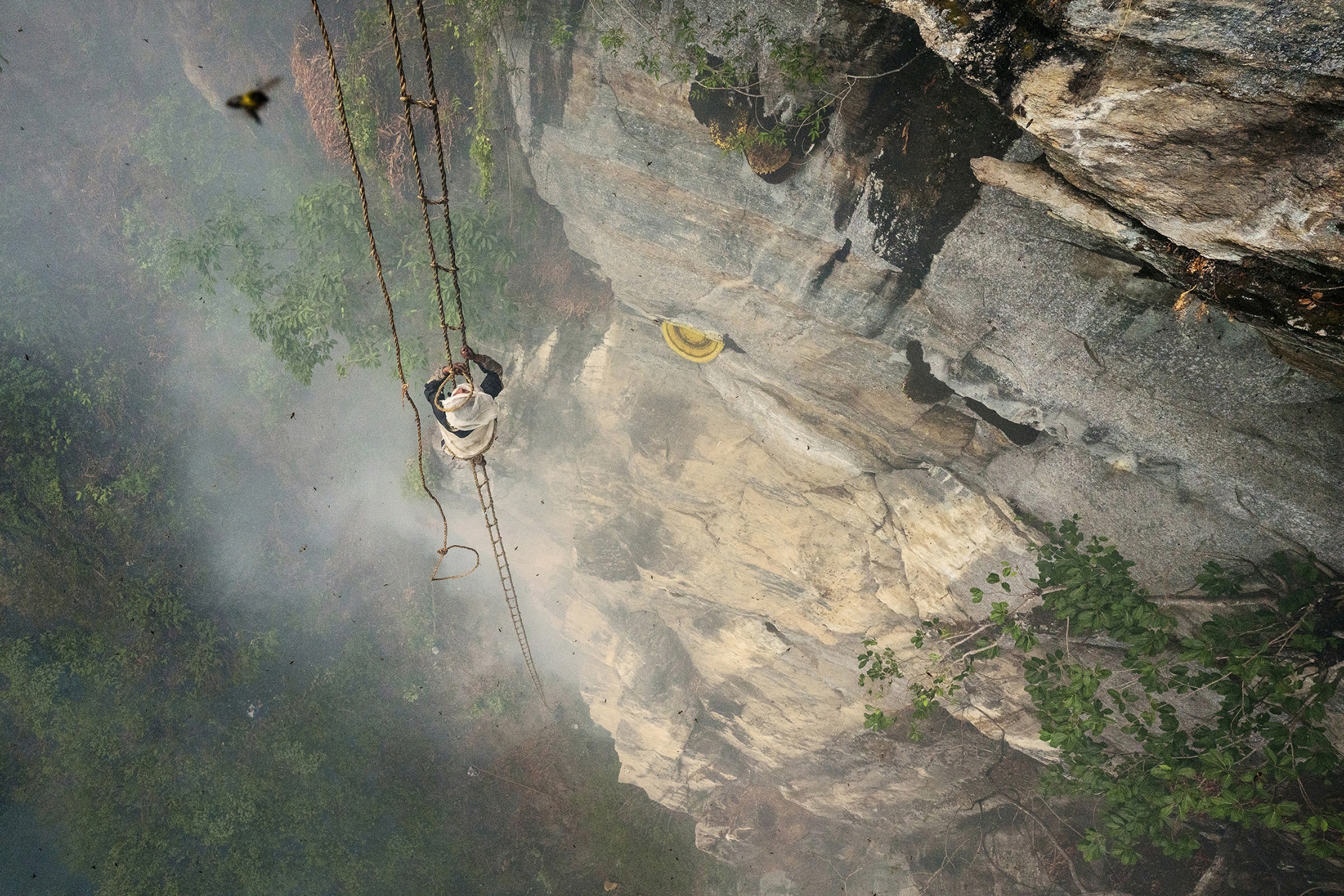 a man climbing on a rope ladder off a cliff in front of a cloud of smoke