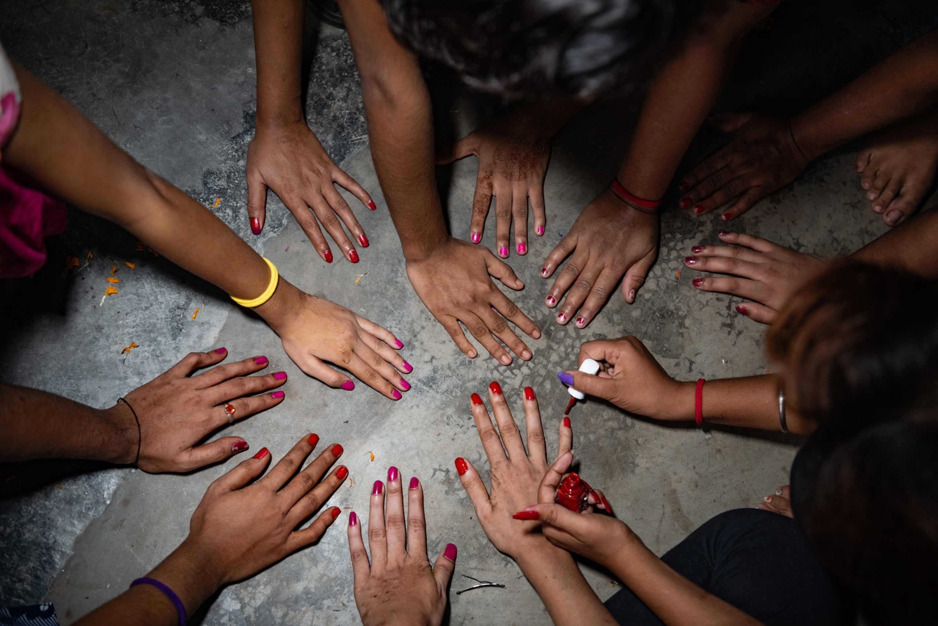 a group of hands on concrete all with red nailpolish