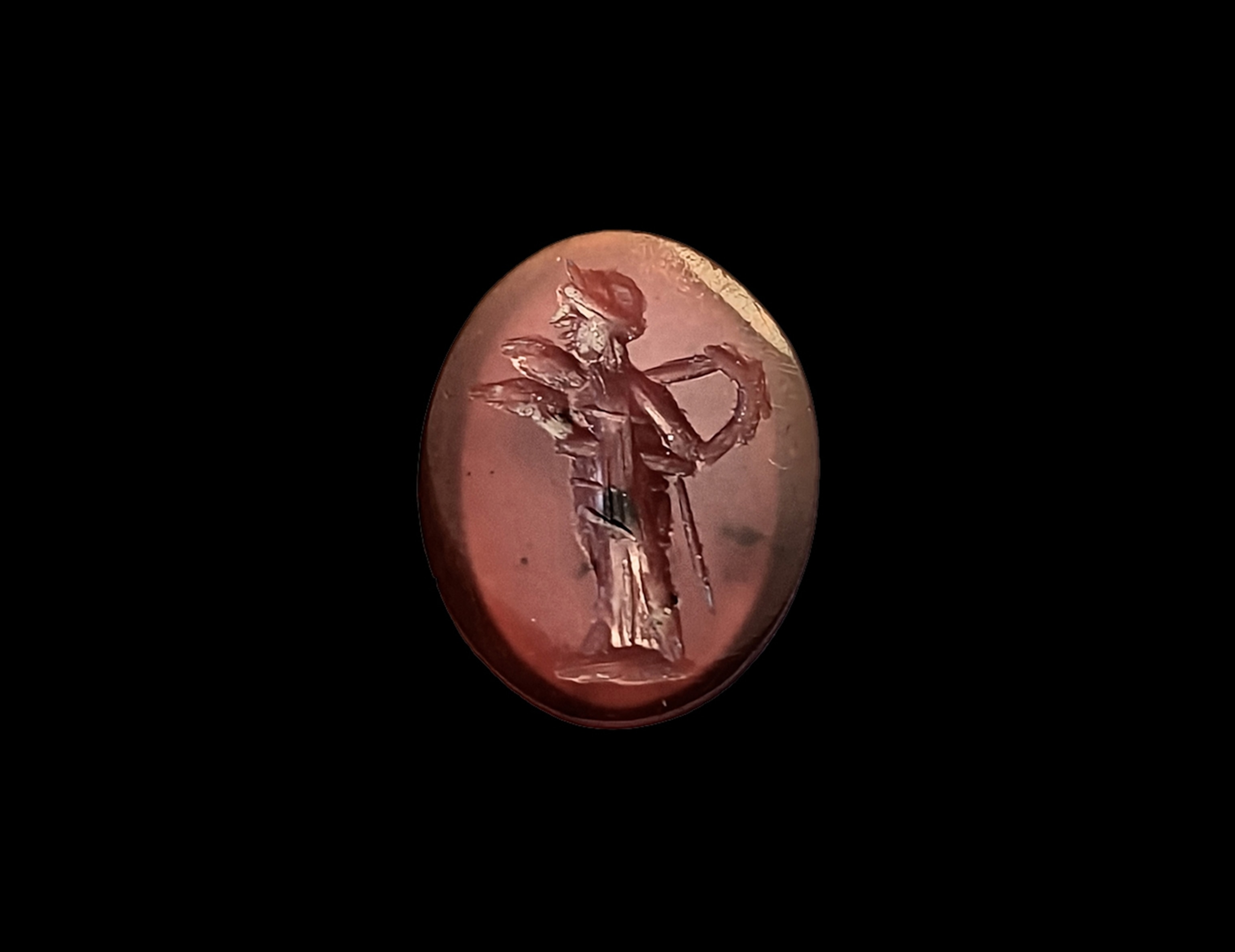 Diana, drawing an arrow from her quiver(?) The goddess here wears a long chiton instead of her usual short tunic. Diana usually holds a bow, lacking here, though a staff seems to project below her left arm. Two protuberances in front of the upper part of her body are hard to explain, except as an initial bow, lacking here, though a staff seems to project below her left arm. Two protuberances in front of the upper part of her body are hard to explain, except as an initial mistake by the gem-cutter. Ground line. Cornelian. This is a rare type because Diana is normally portrayed on gems wearing a short tunic explain, except as an initial mistake by the gem-cutter. Ground line. Cornelian. This is a rare type because Diana is normally portrayed on gems wearing a short tunic suitable for hunting as Henig. gems wearing a short tunic suitable for hunting as Henig.
