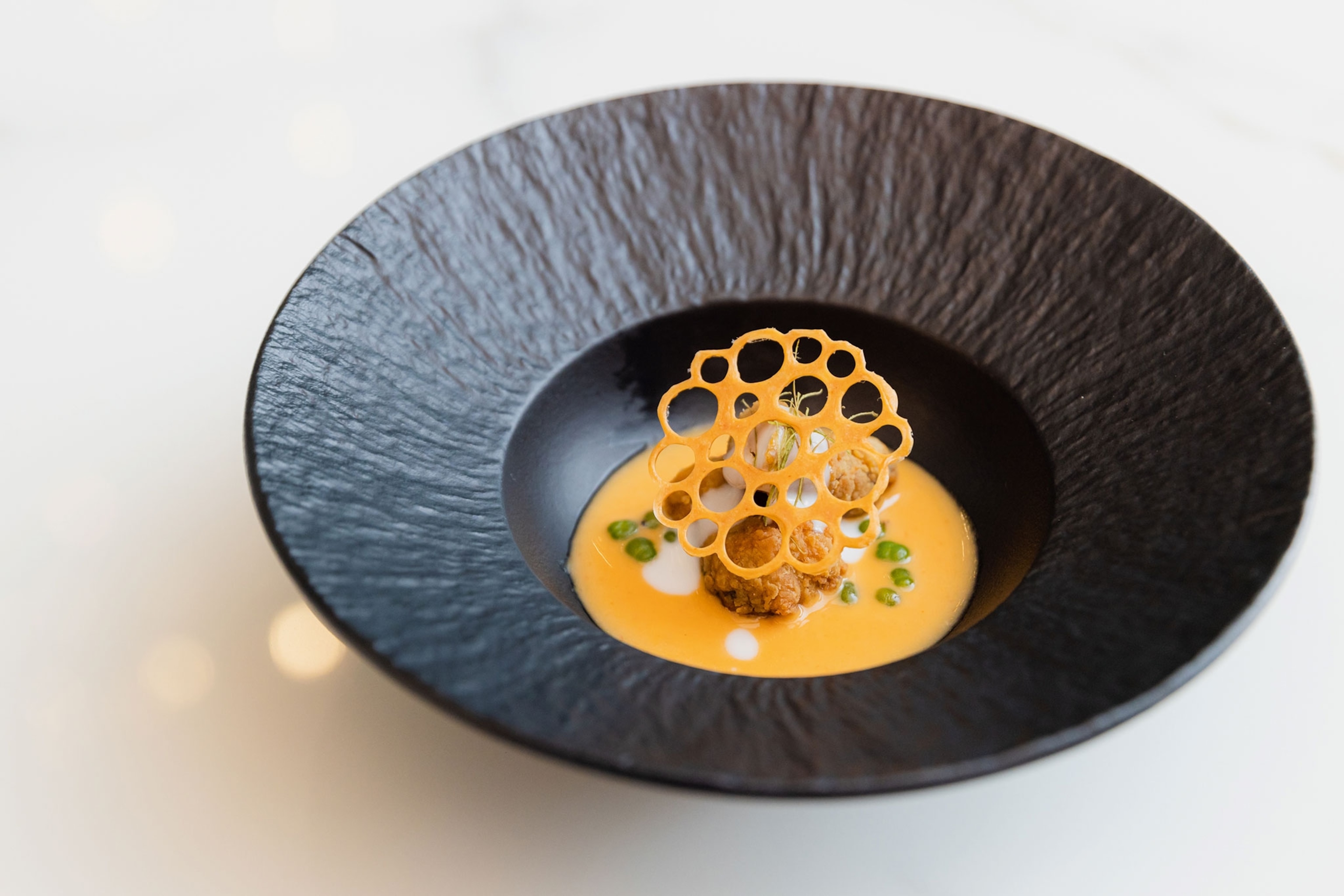 Mango-coloured curry in a black bowl.