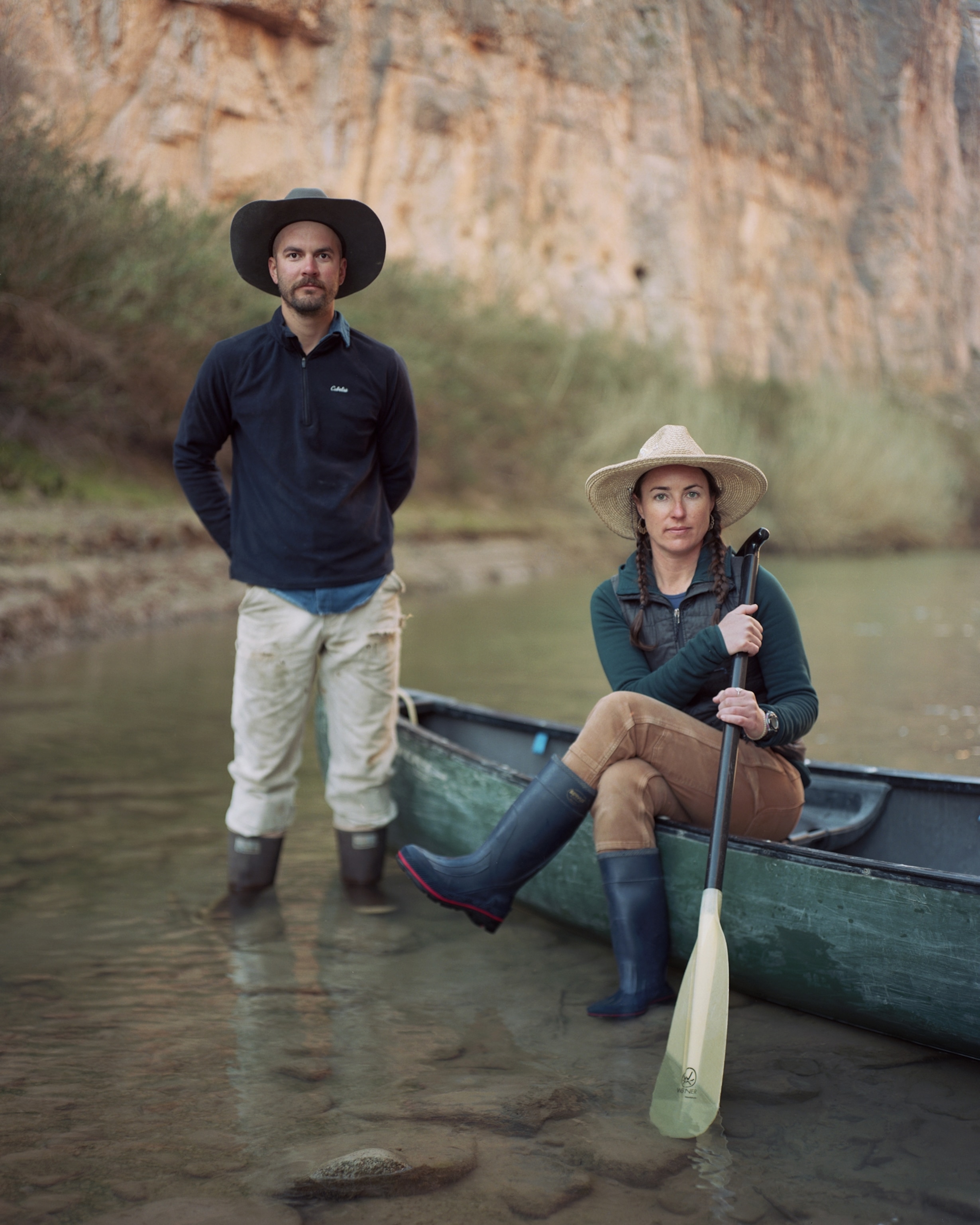 Picture of woman with paddle sitting on canoe and man standing in water next to it.