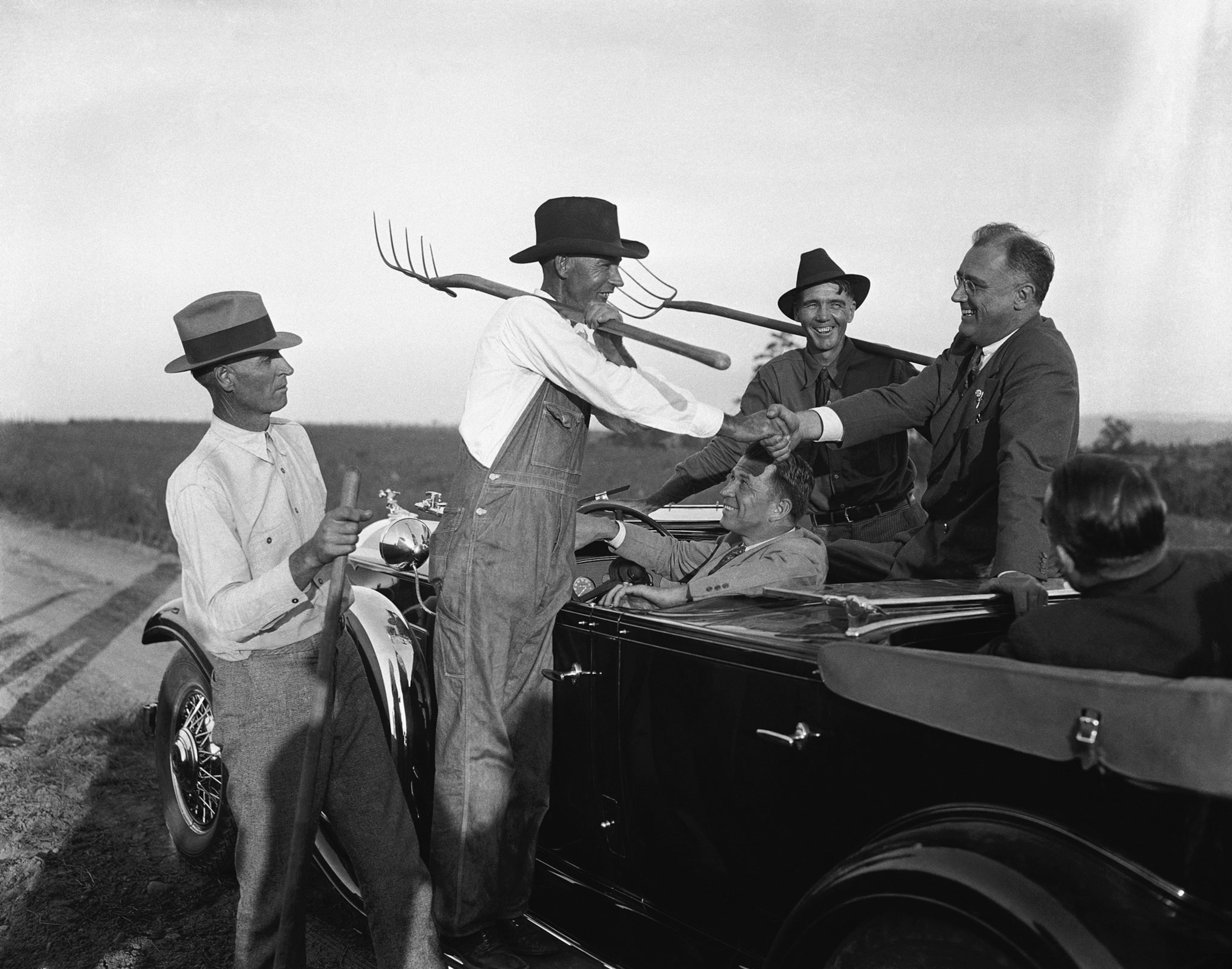 a presidential candidate shaking hands with farmers holding pitchforks