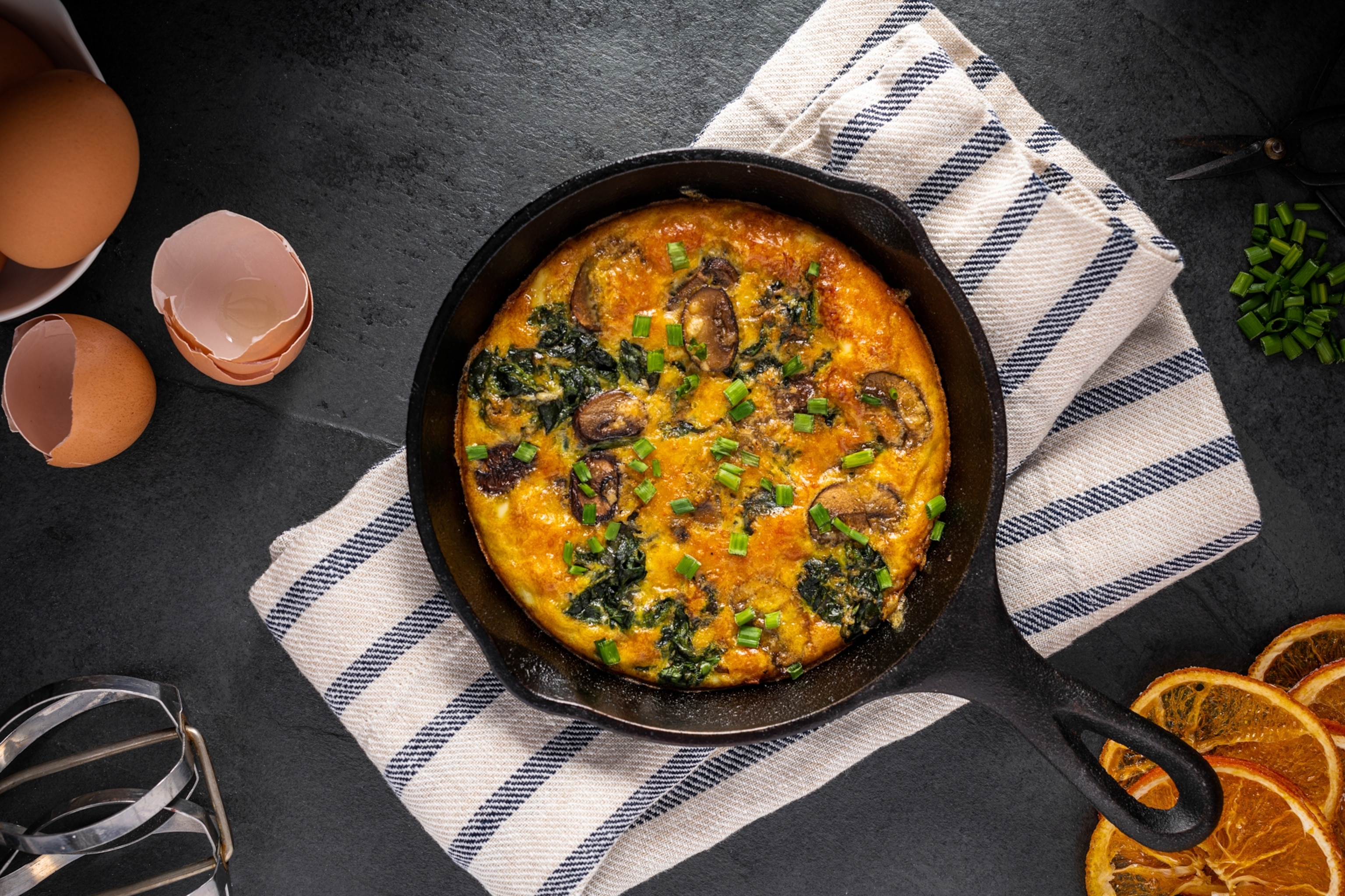 Frittata with spinach, mushrooms, and parmesan cheese garnished with chopped chives viewed from above.