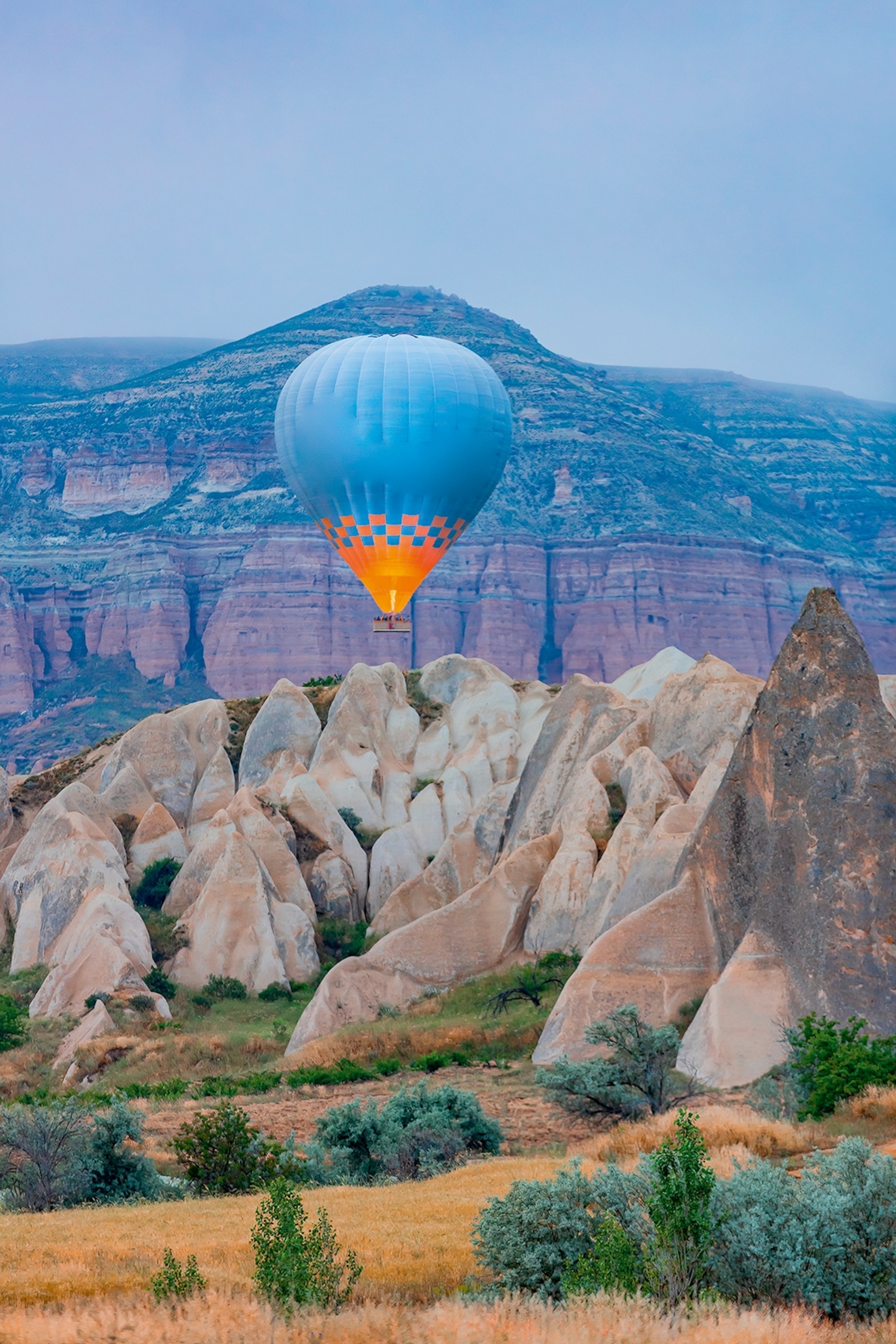 Hot air balloon flies over rock formations against a backdrop of mountains