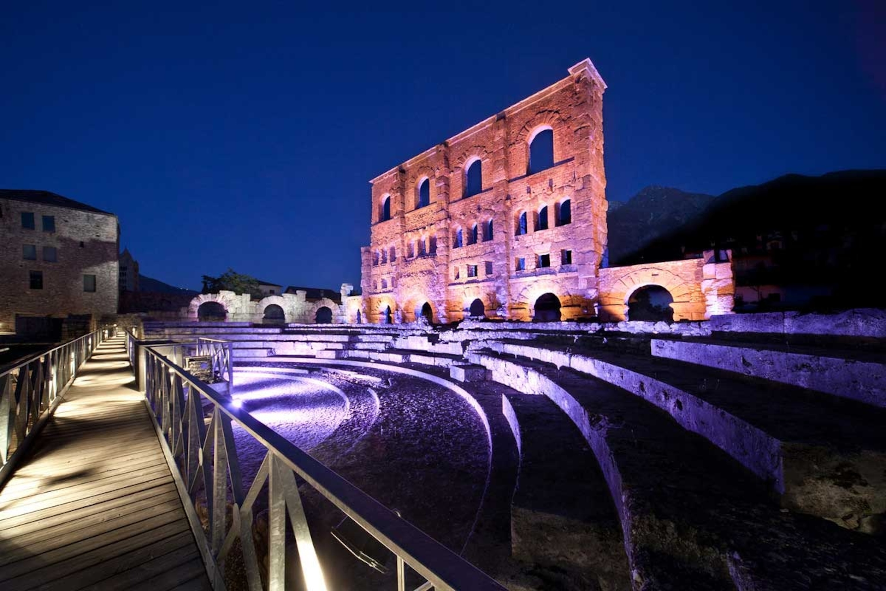 A ruined wall of a Roman theatre, lit from below by coloured lights