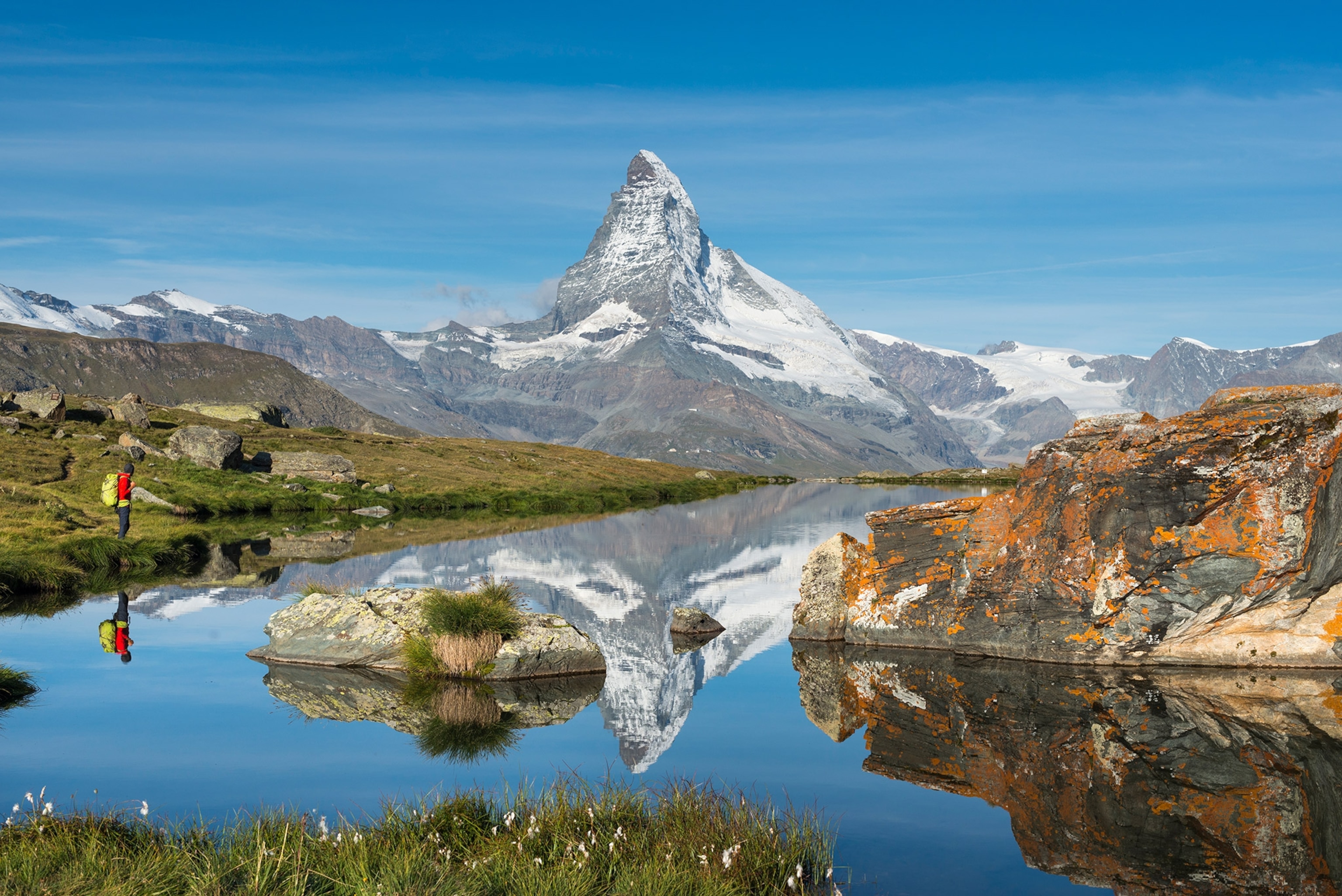 A man stands as a mountain in reflected into a lake.