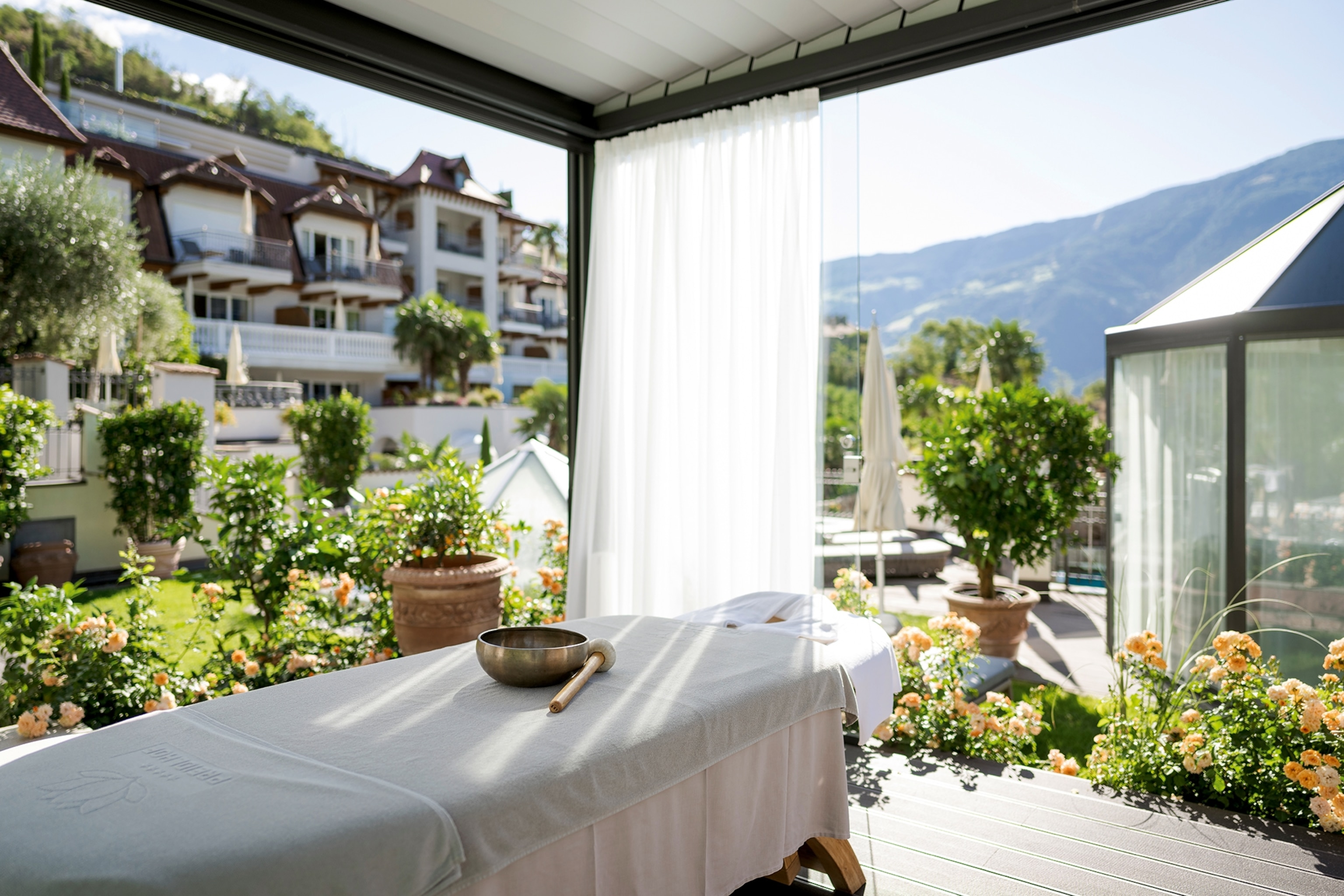 The corner of a panoramic room with views on greenery and hills, a massage bed just in front.