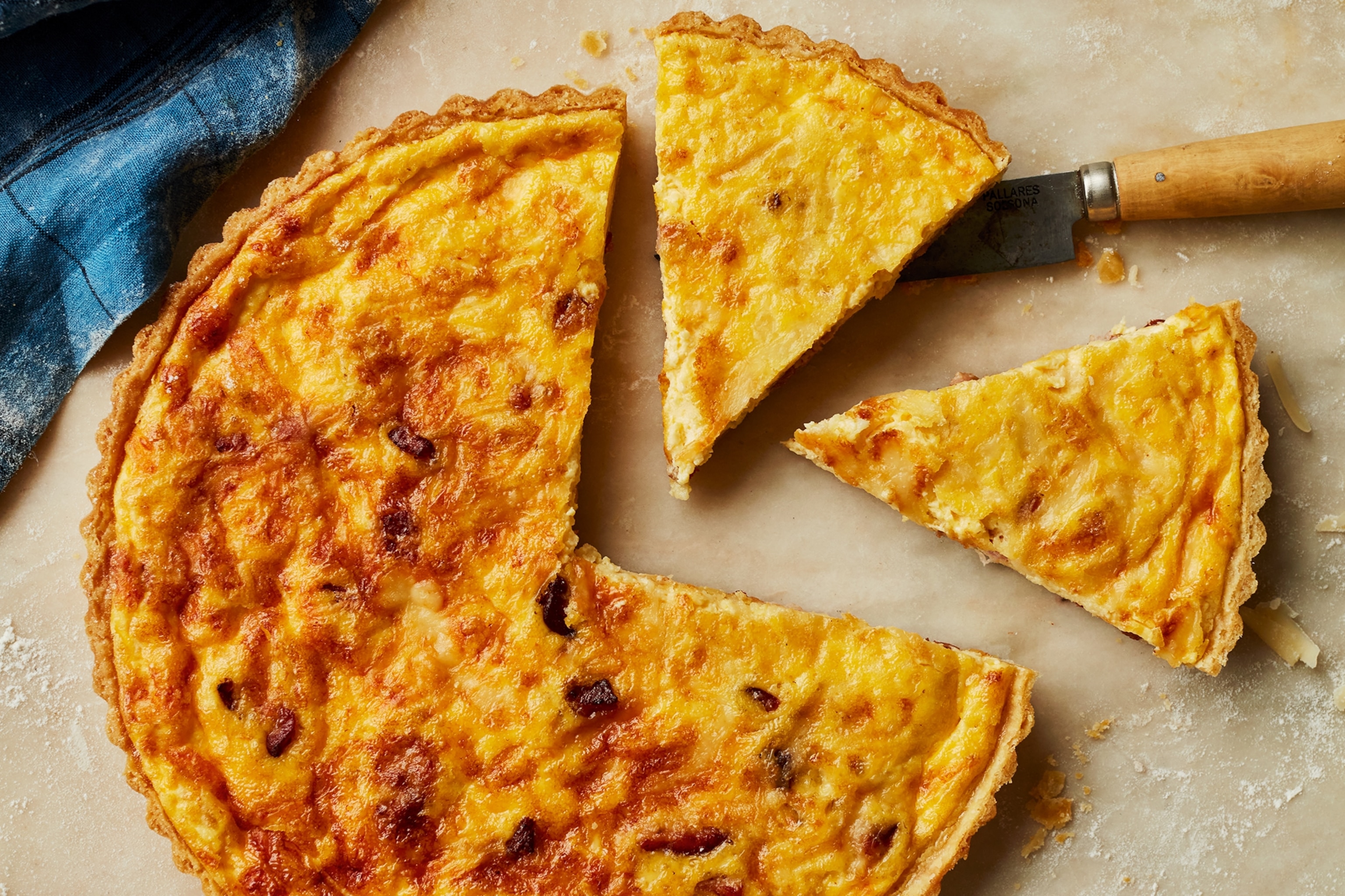A quiche lorraine with two cut slices which is sitting on a milky white coloured marble countertop