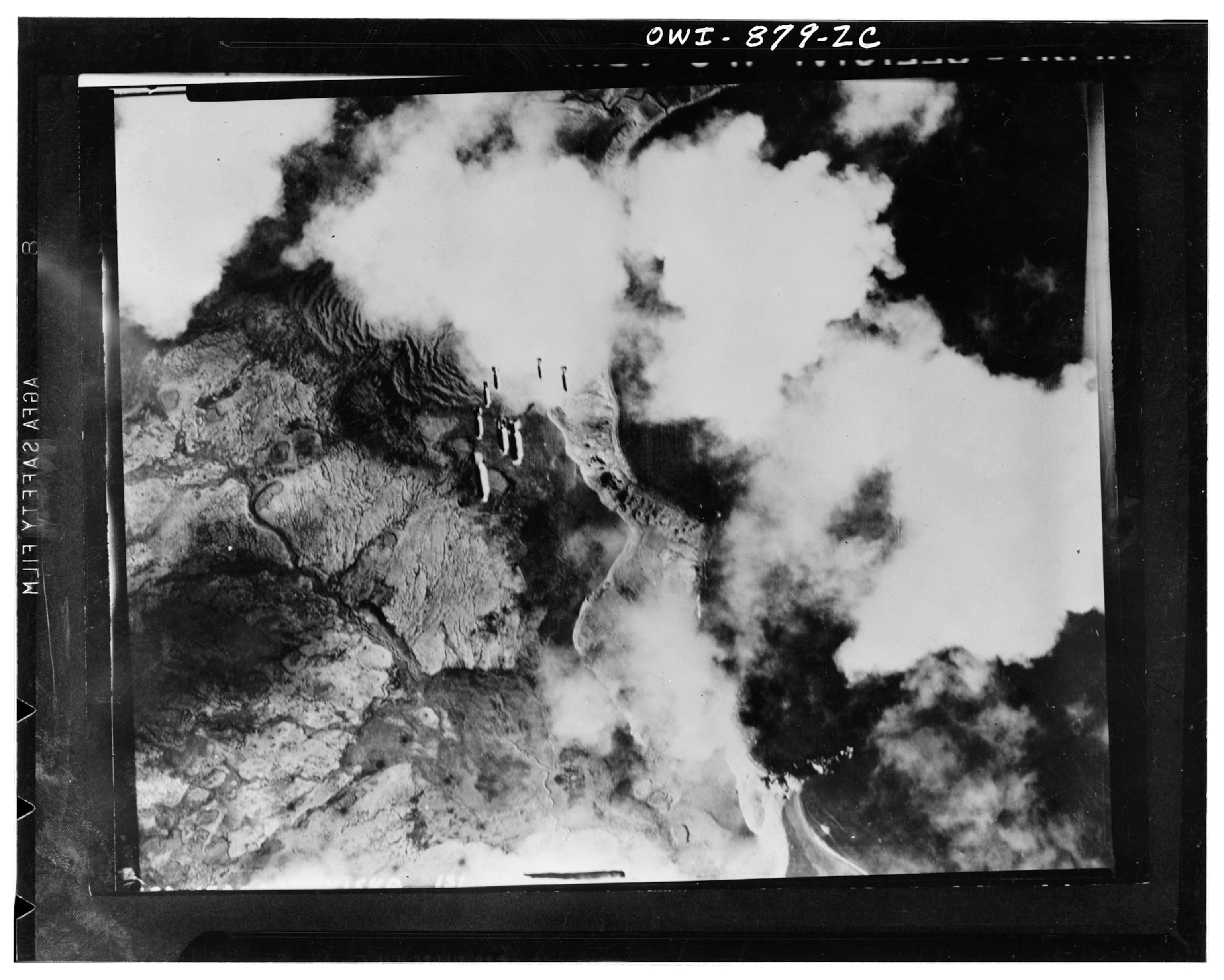 An aerial looking over an island with a several bombs seen close together as they fall towards the ground below.