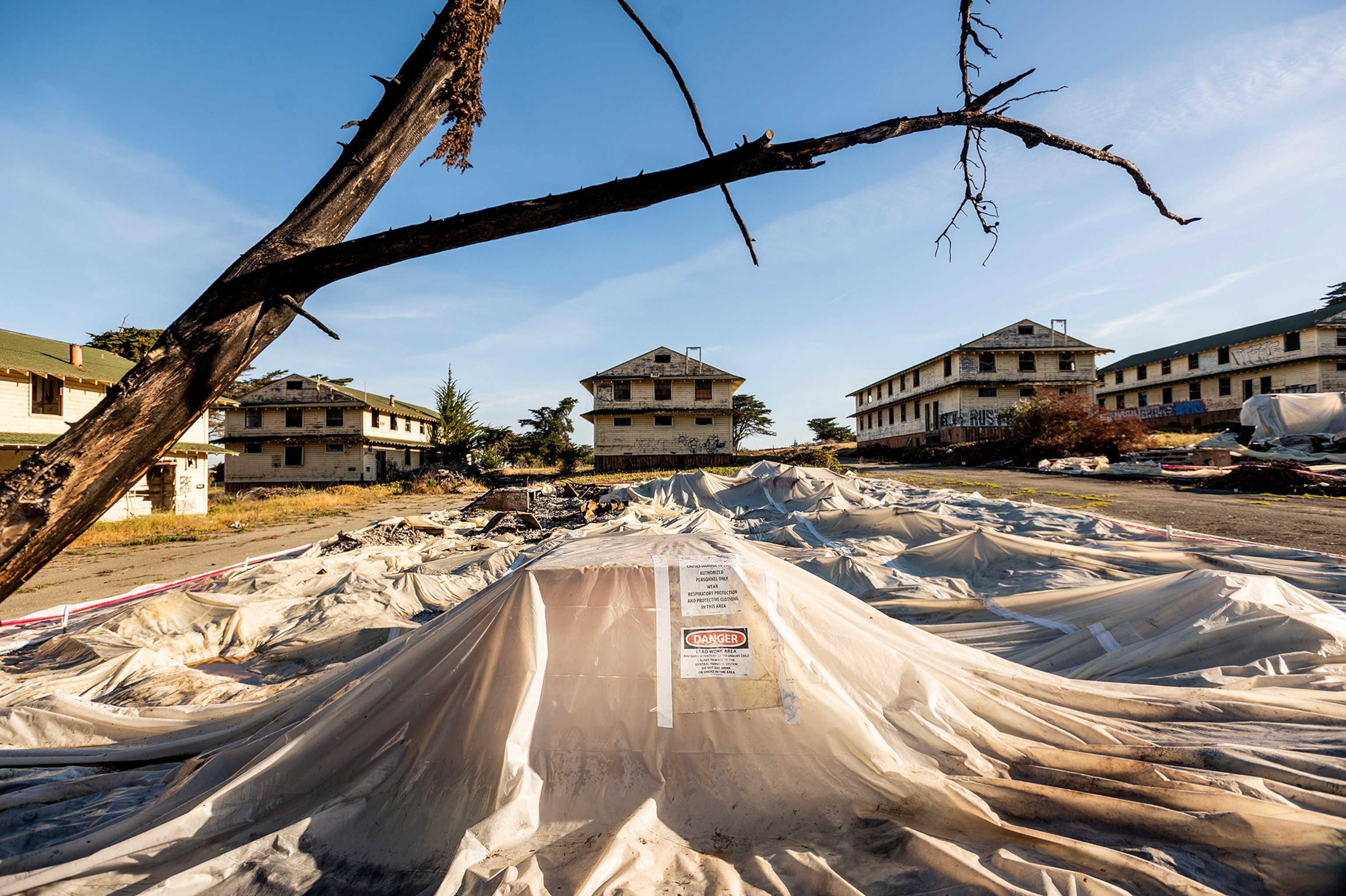 A tarp covers debris in the foreground and a variety of abandoned and desolate builds in the background.