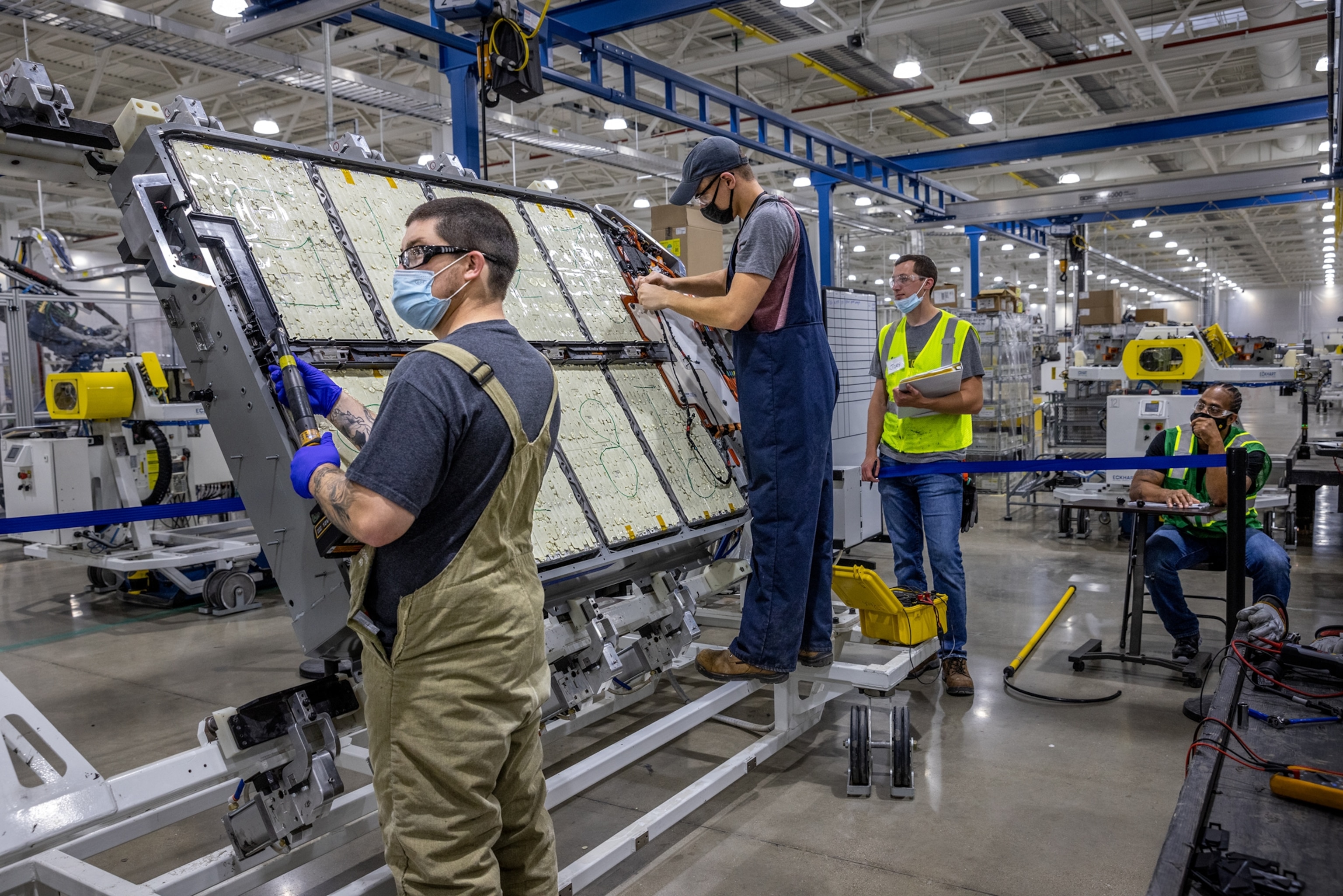 Picture of workers in face masks constructing a truck battery pack on the floor of the factory .