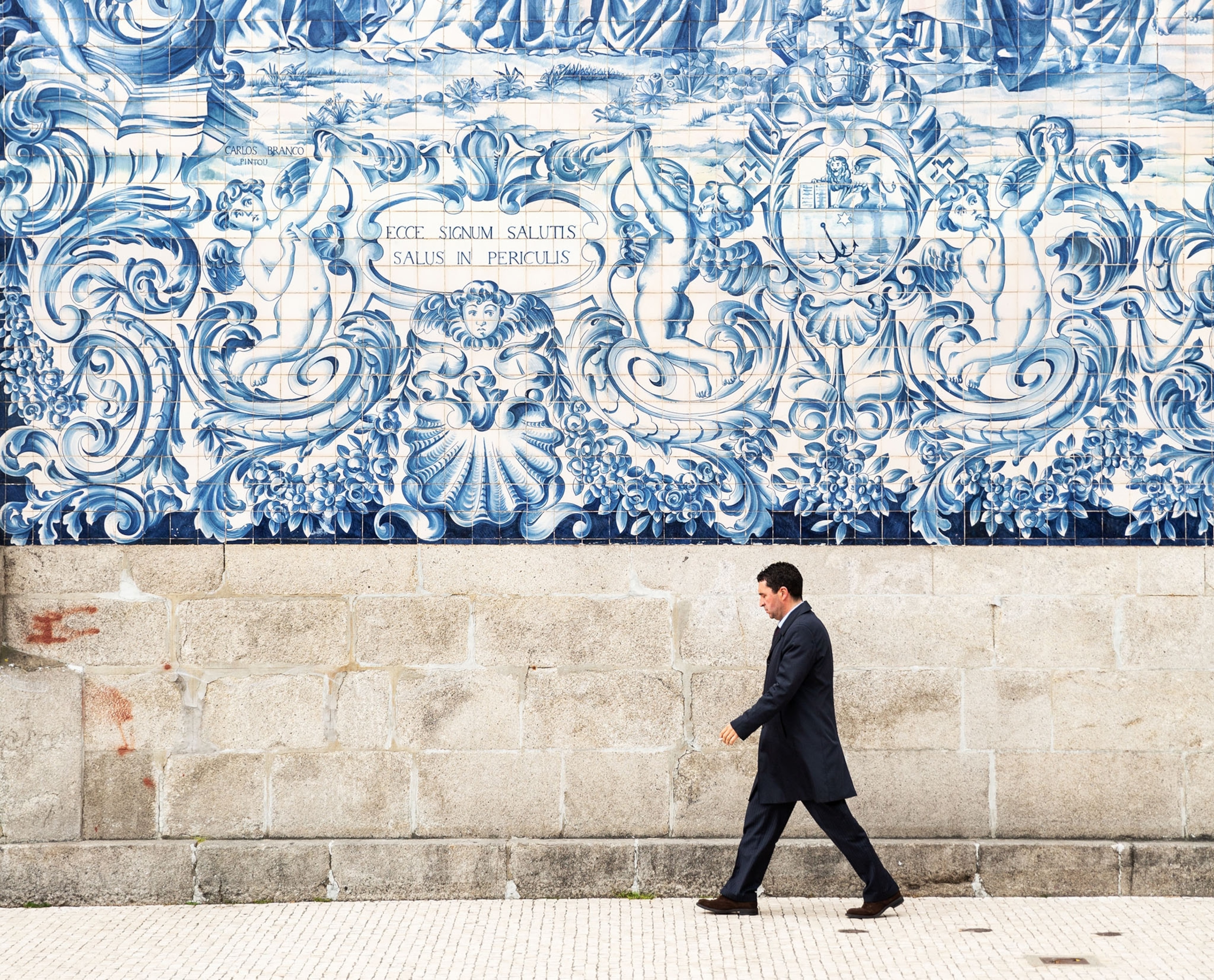 a man walking by a wall covered in elaborate blue tiles