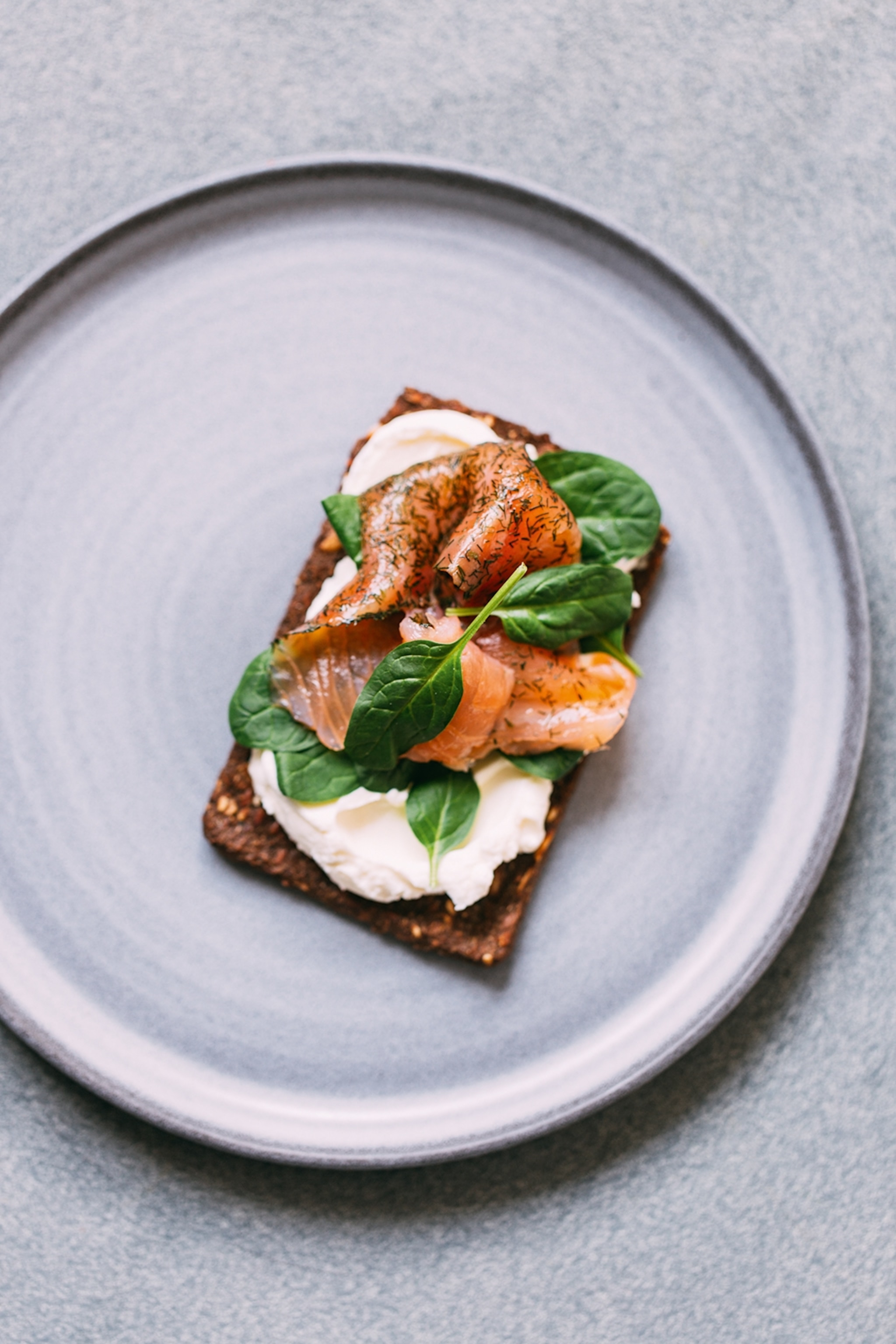 Piece of rye bread on a plate with cream cheese, spinach and salmon on top
