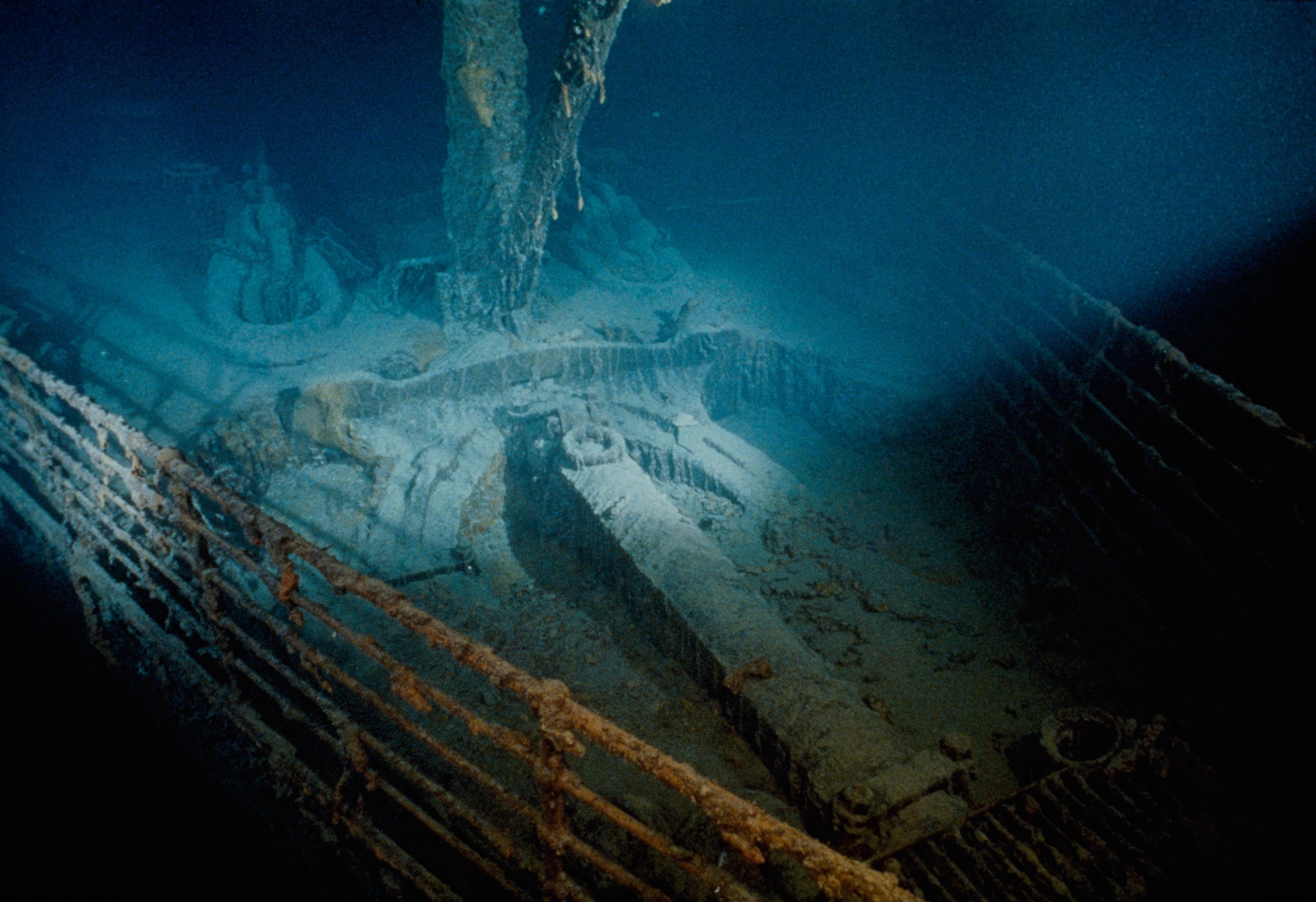 Overhead view of the front of the Titanic ship underwater, covered in the elements of the ocean with light shining from the right side of the frame onto the ship.