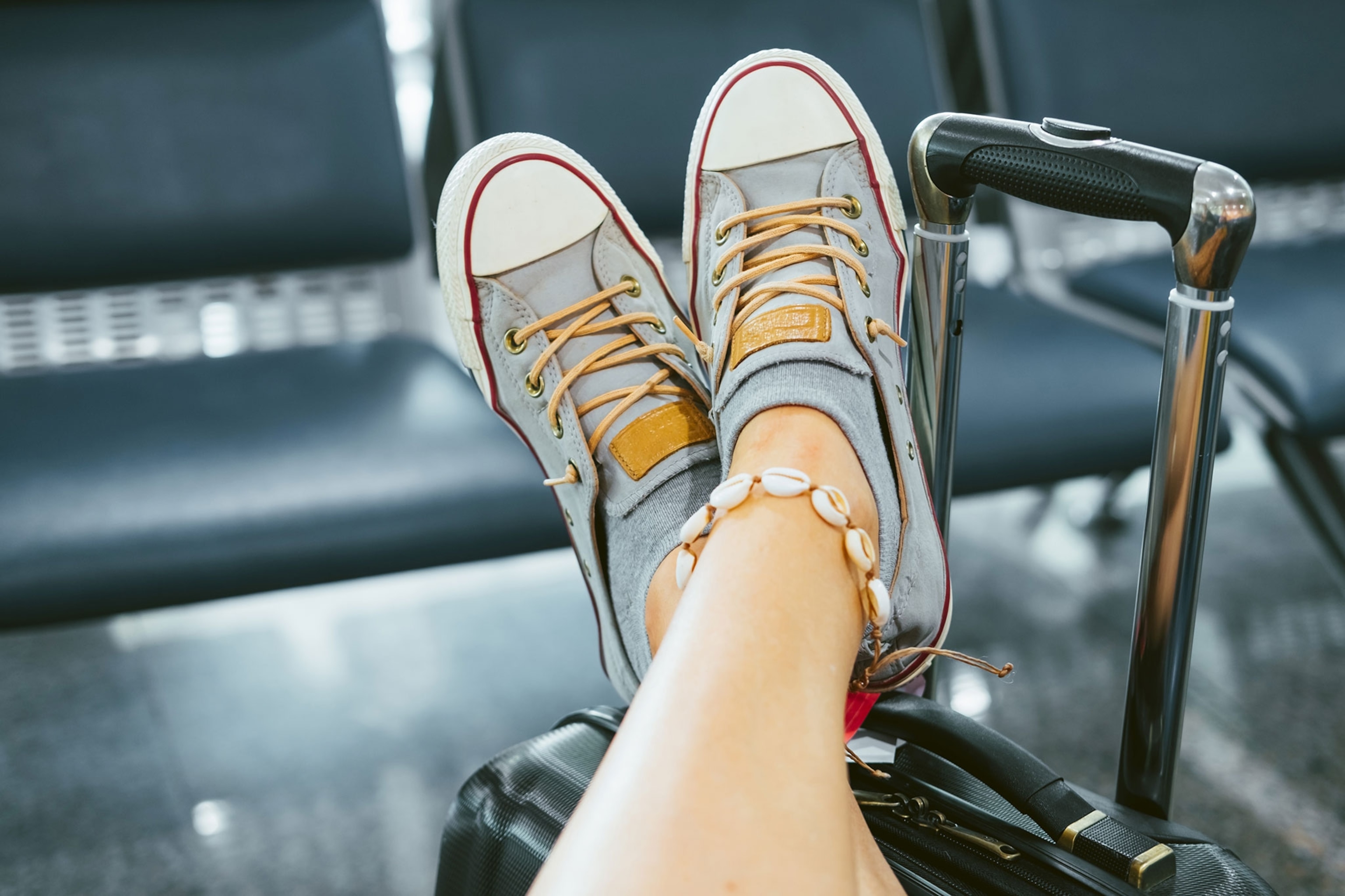 A person's feet wearing grey slip-on sneakers resting on a suitcase in an airport.