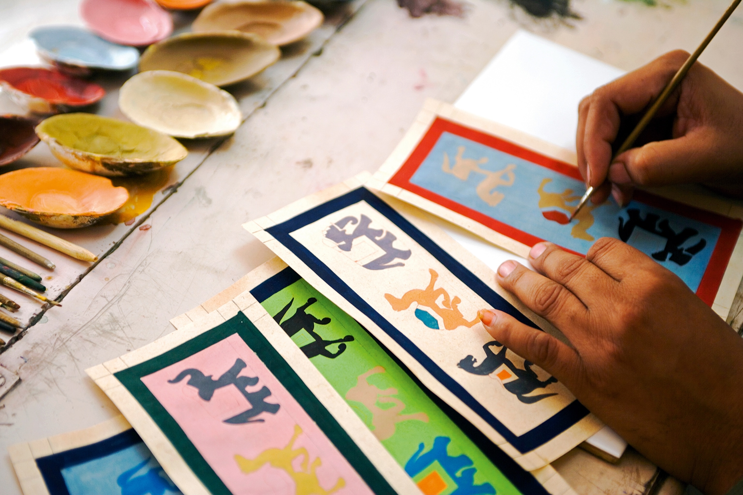 Hands painting coloured symbols onto paper