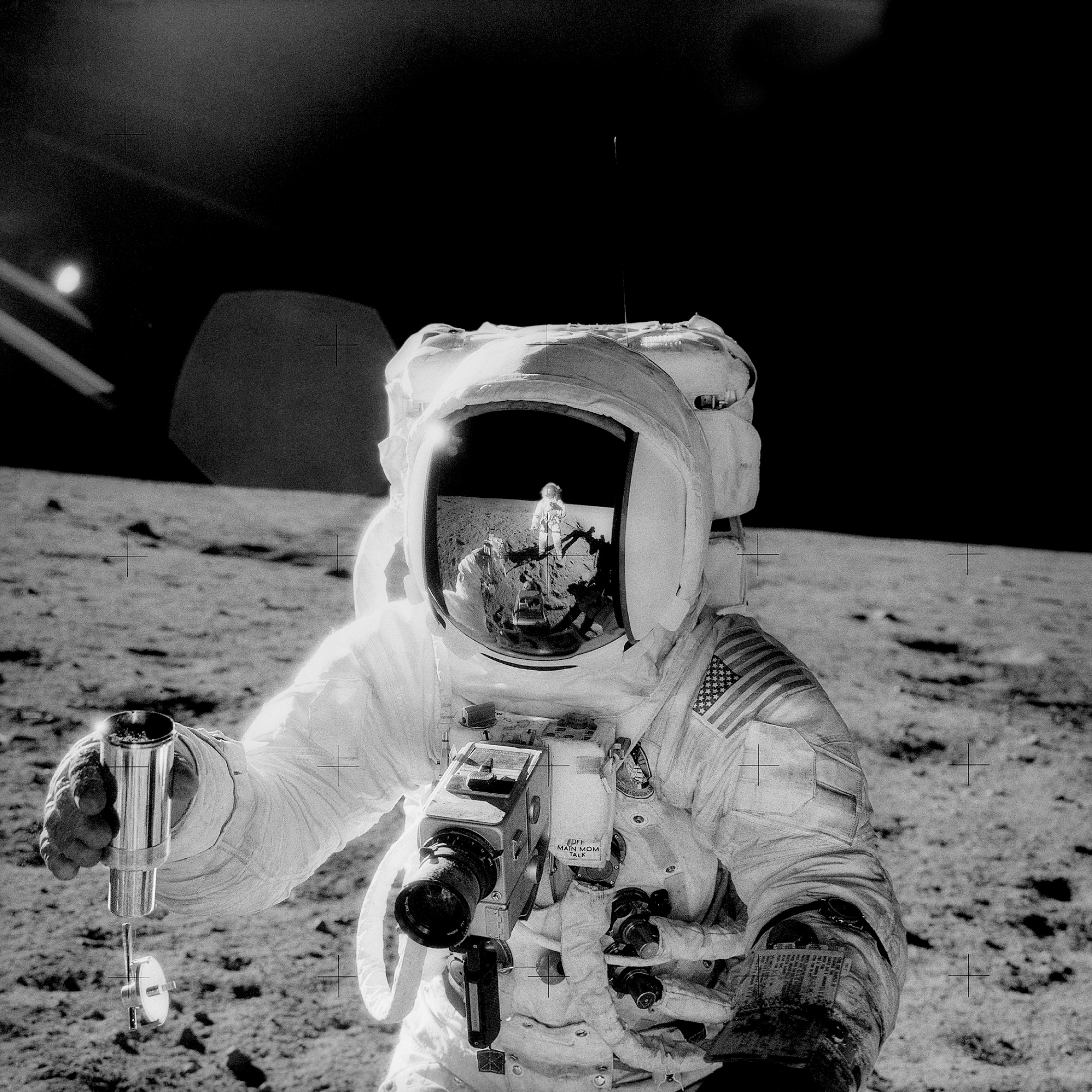 Picture of astronaut in space suit on Moon surface and reflection of another on in his helmet visor.