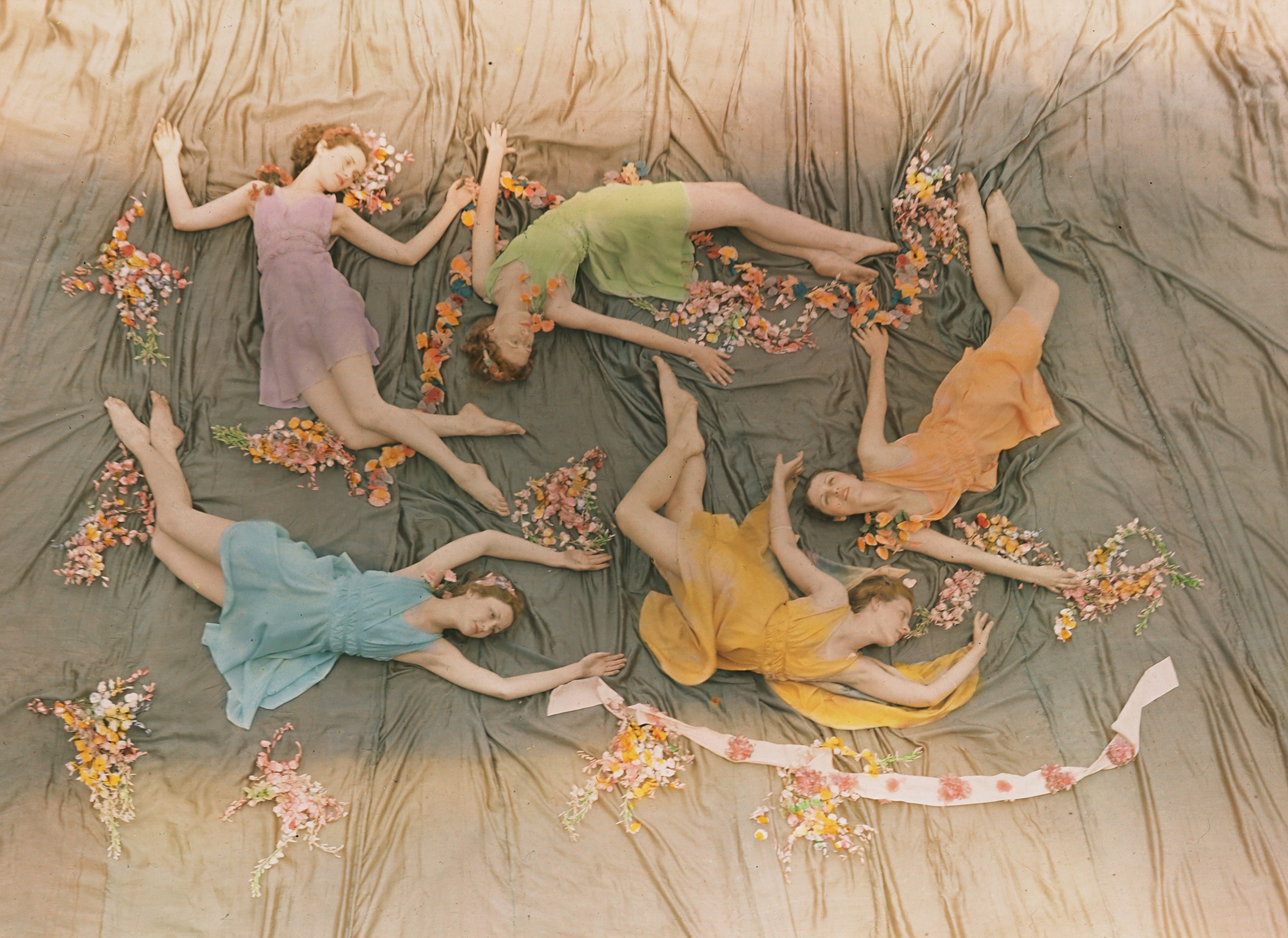 five young women in pastel-colored dresses laying on draped floor forming beautiful group.