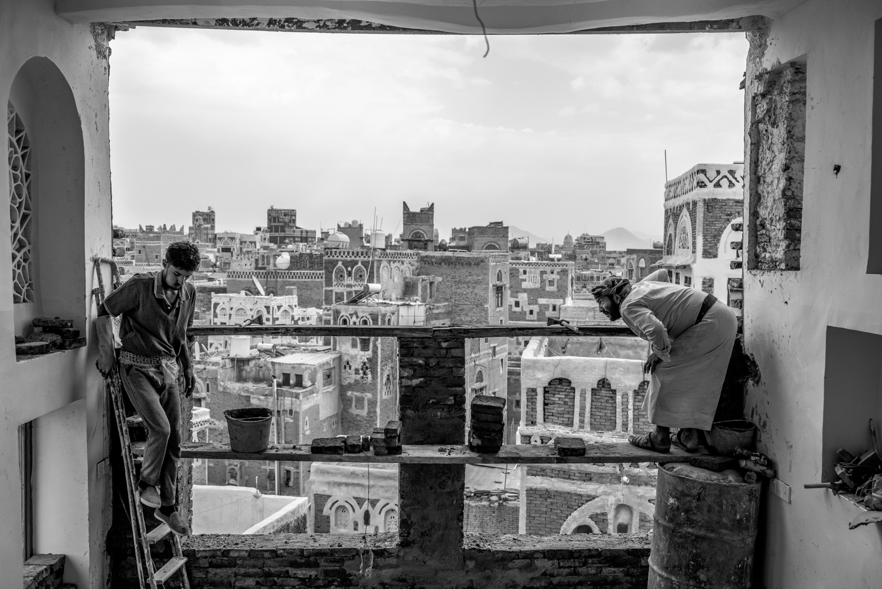 Picture of two men leveling a plank in window opening with old city on the background.