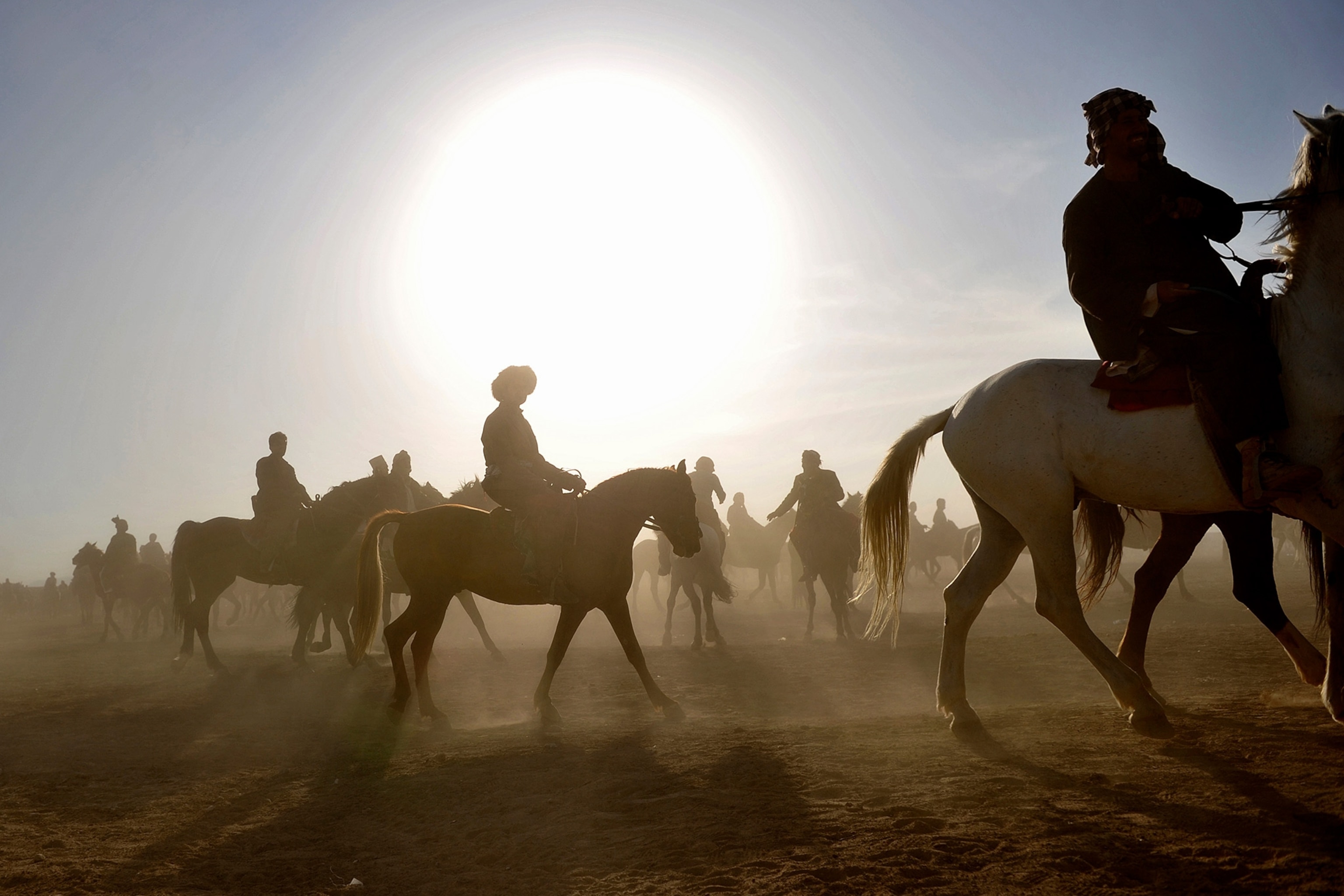 Men on horses are silhouetted by a bright sun on horses.