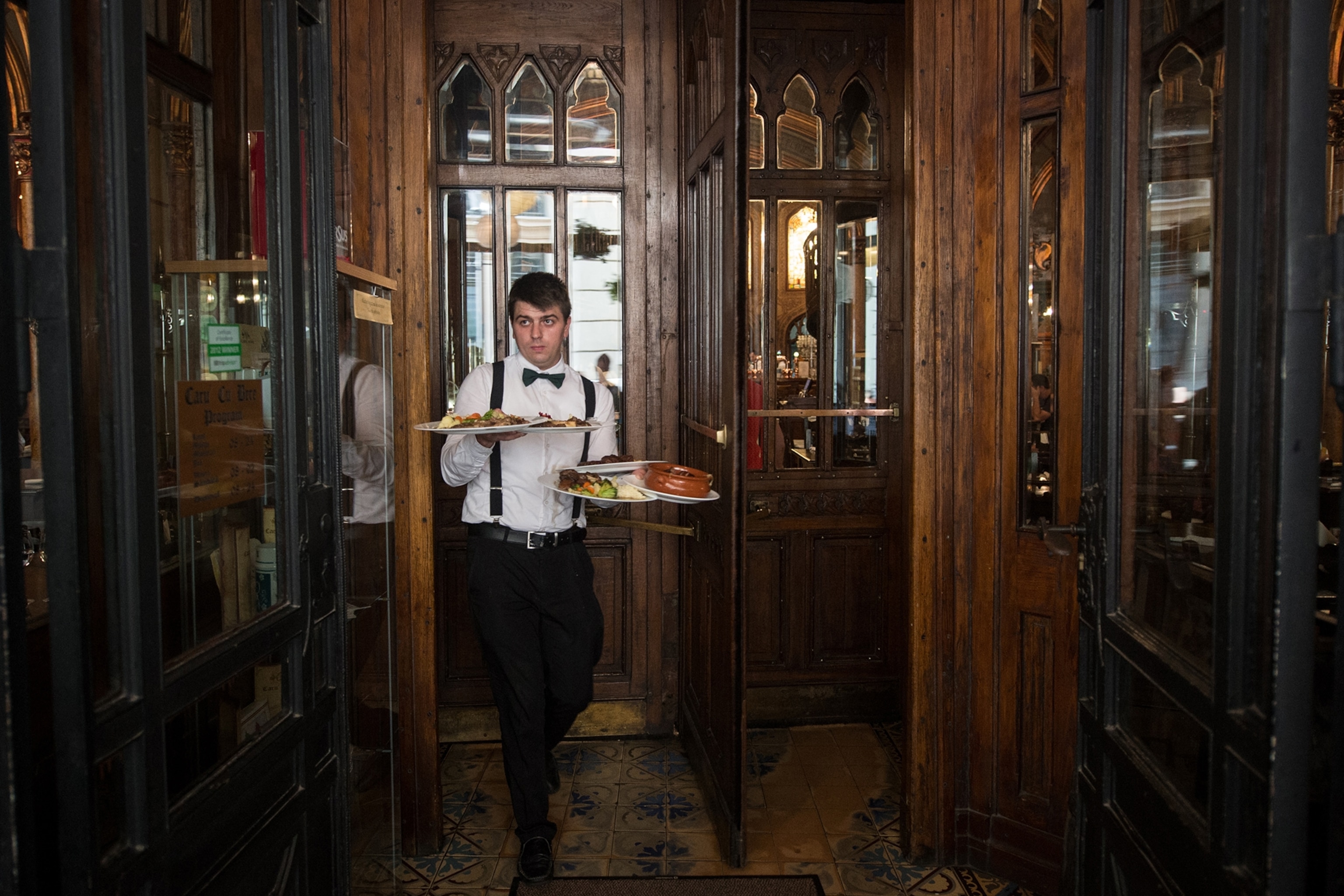 In this photo taken Monday, July 31, 2014, a waiter carries plates with food to customers at Caru cu Bere restaurant, Bucharest, Romania. Caru cu Bere, a fabled restaurant in the Old City, has been serving cold beer, spicy sausages and a lot more since the last year of the 19th century.