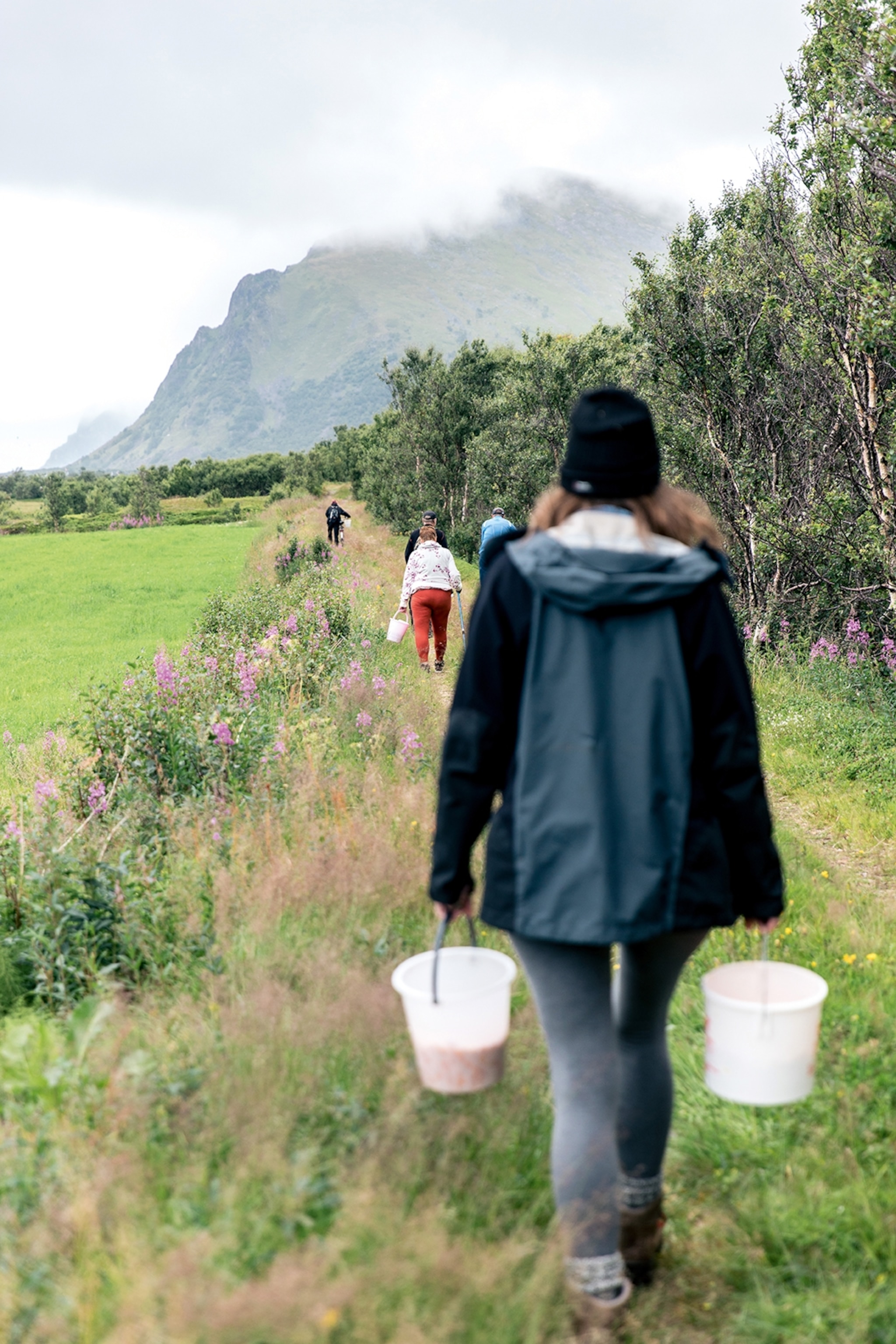 a woman walking through a field with buckets in her hands