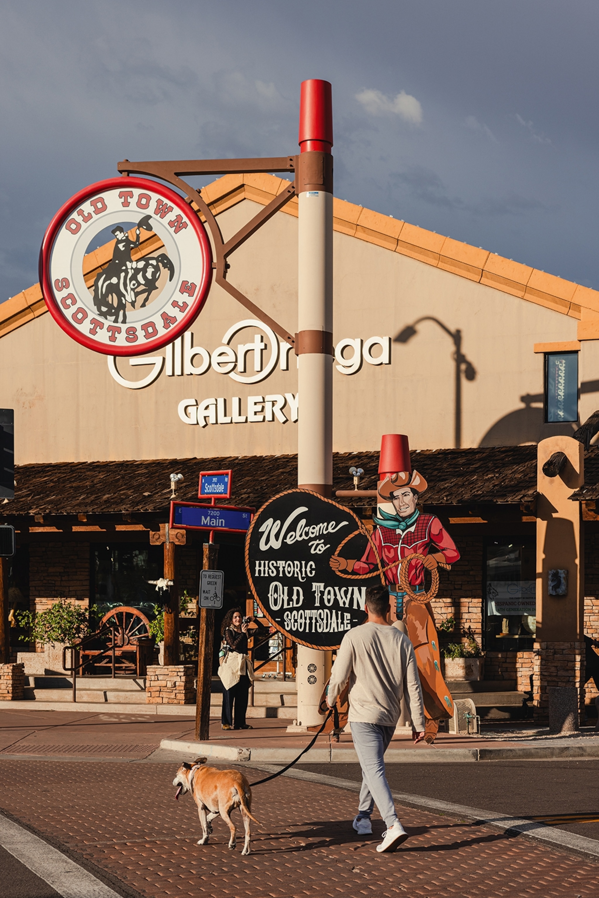 A dog walker in Arizona is walking through the old town, passing one of the city's historic cutout billboards of a cwboy.