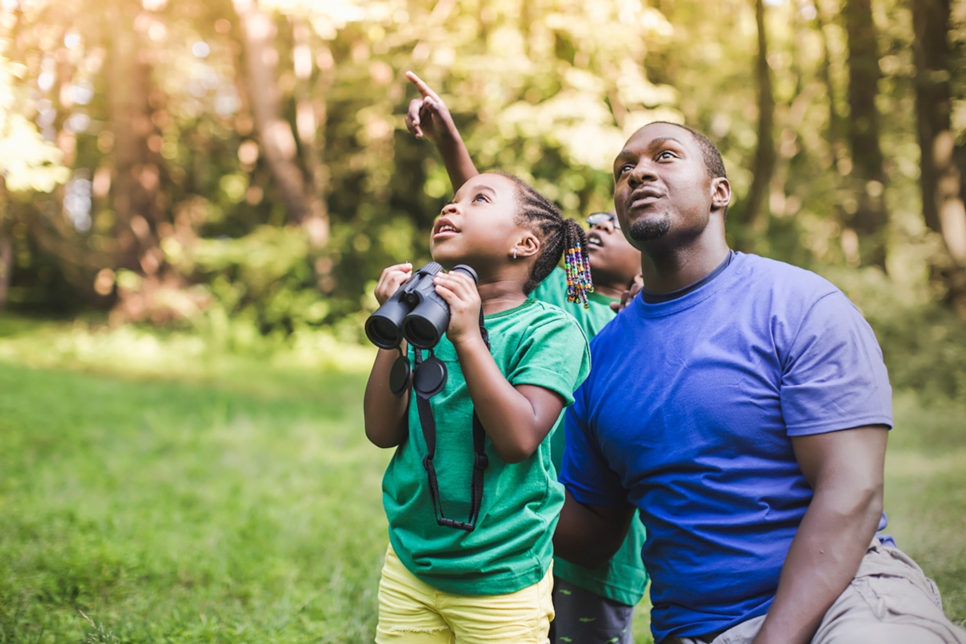 Young father with son and daughter bird watching in eco forest camp.