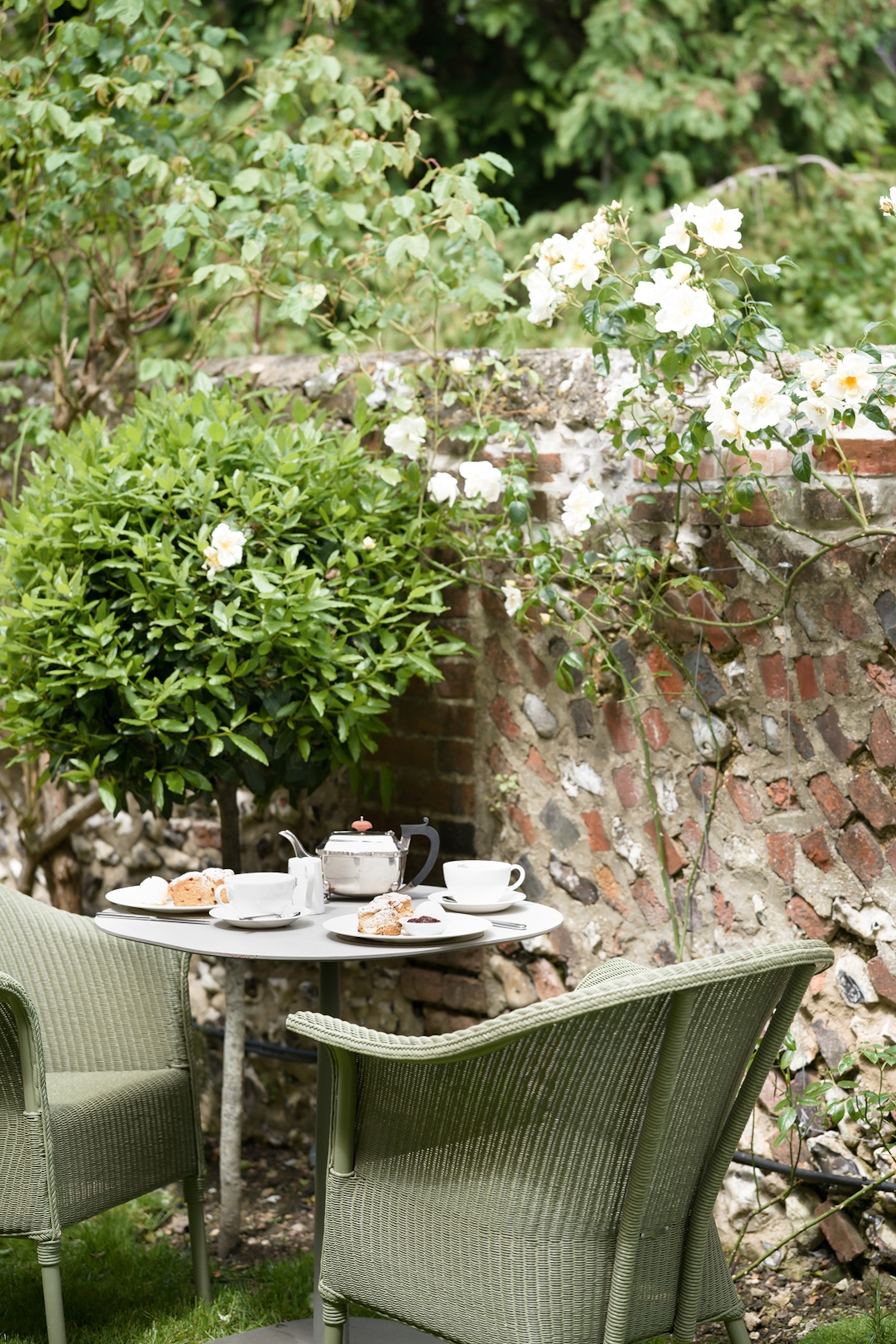 Wicker chairs sat at a table with teacups, a tea pot and scones on plates