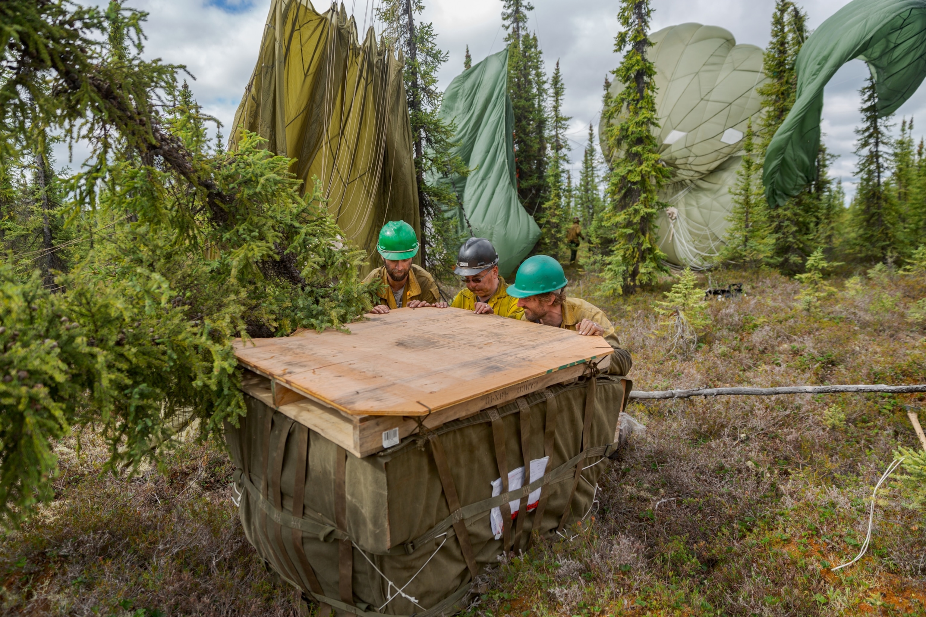 three men pushing the crate and parachutes hanging on threes behind them