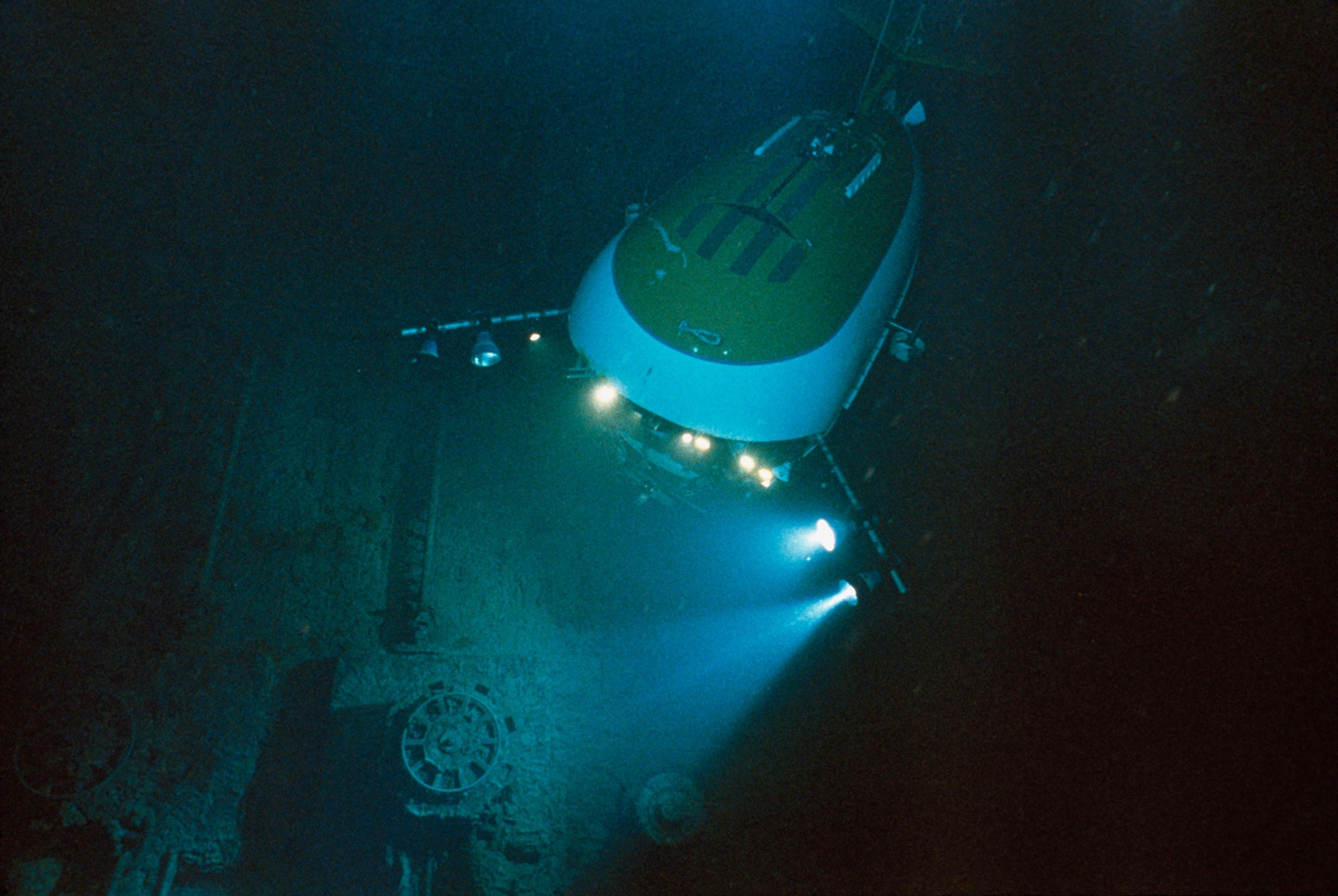 A yellow underwater vehicle shines multiple lights on the deck of the Titanic.