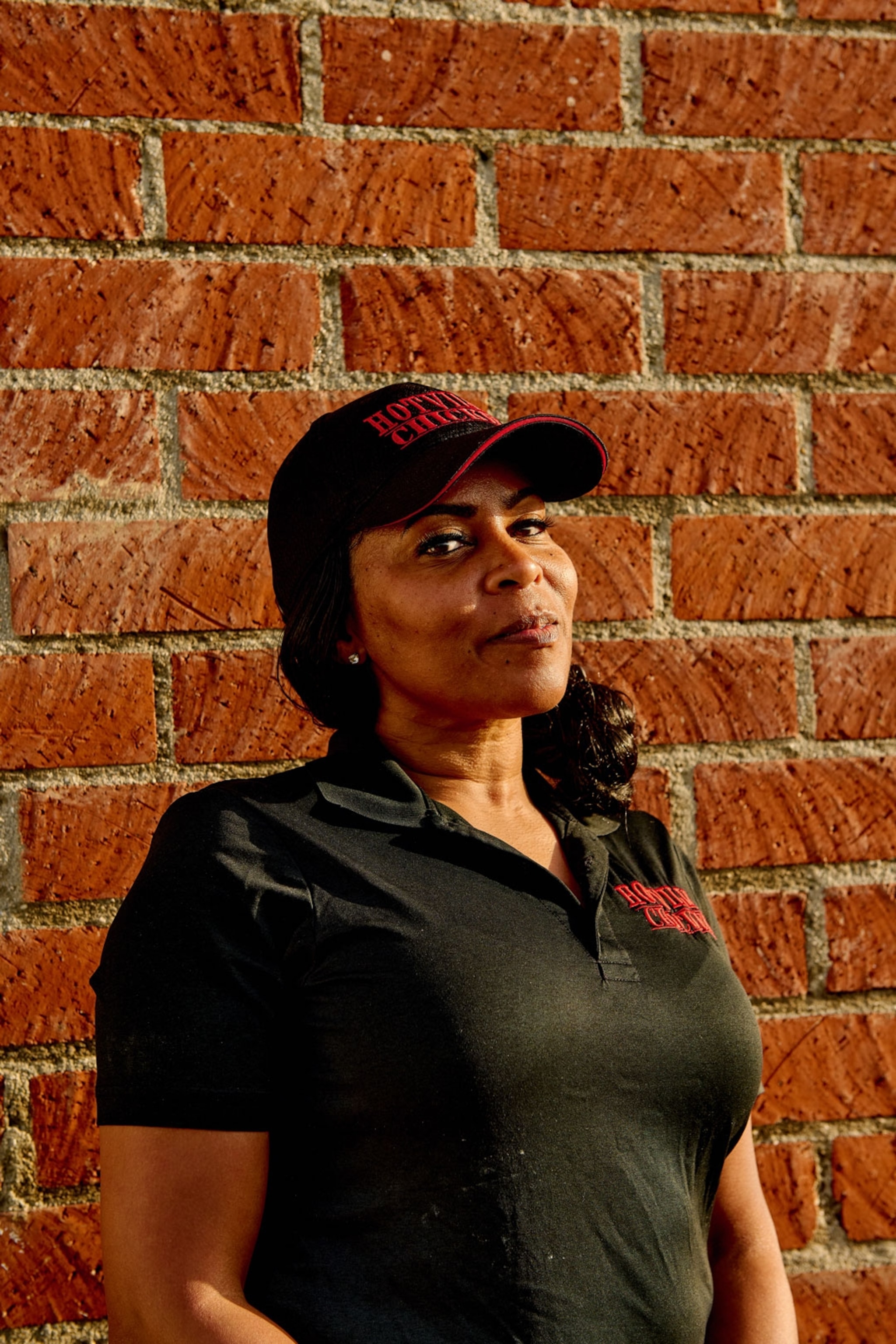 Woman standing against a wall wearing a cap with logo