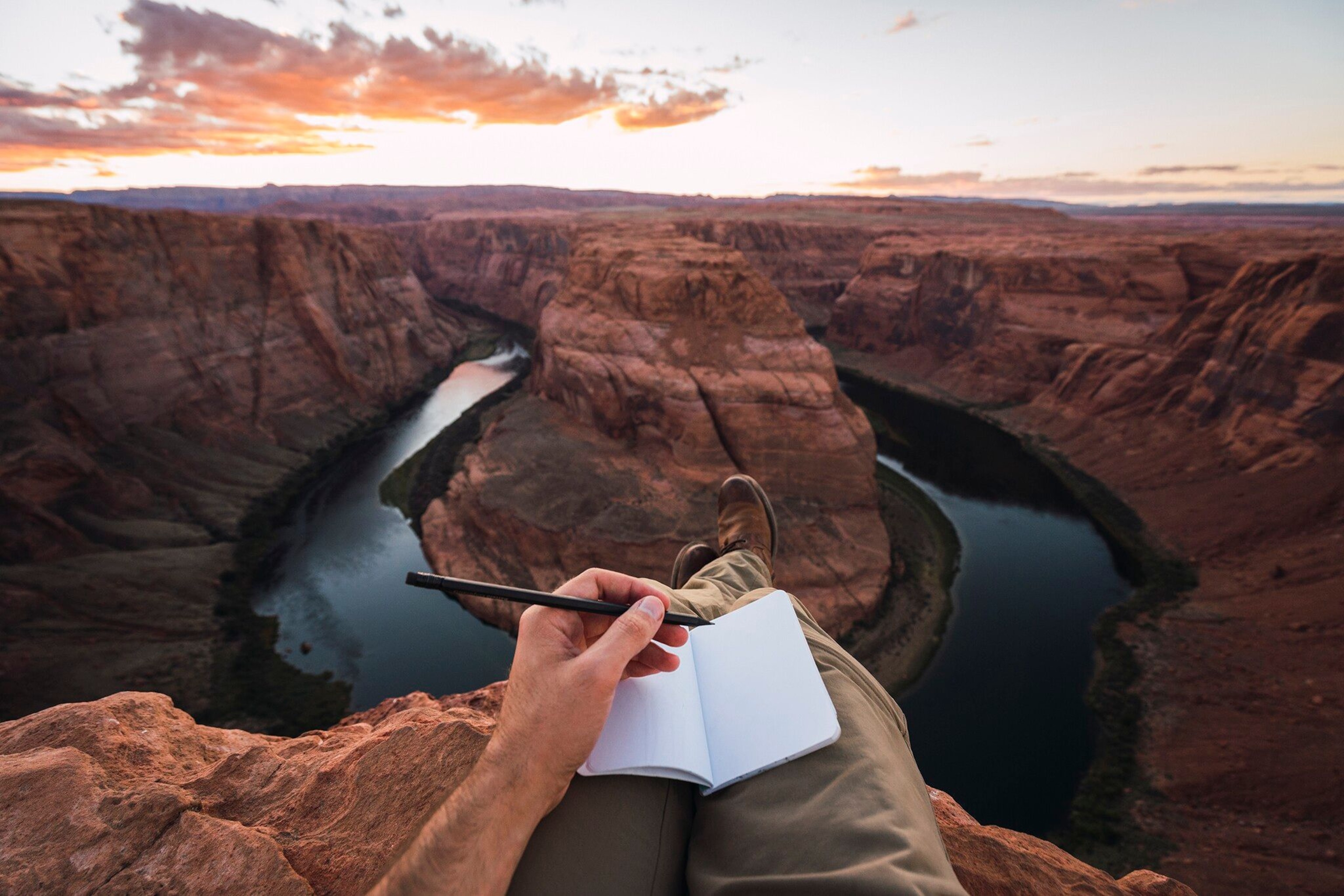 POV of a writer with a pen and notebook sitting next to a canyon.