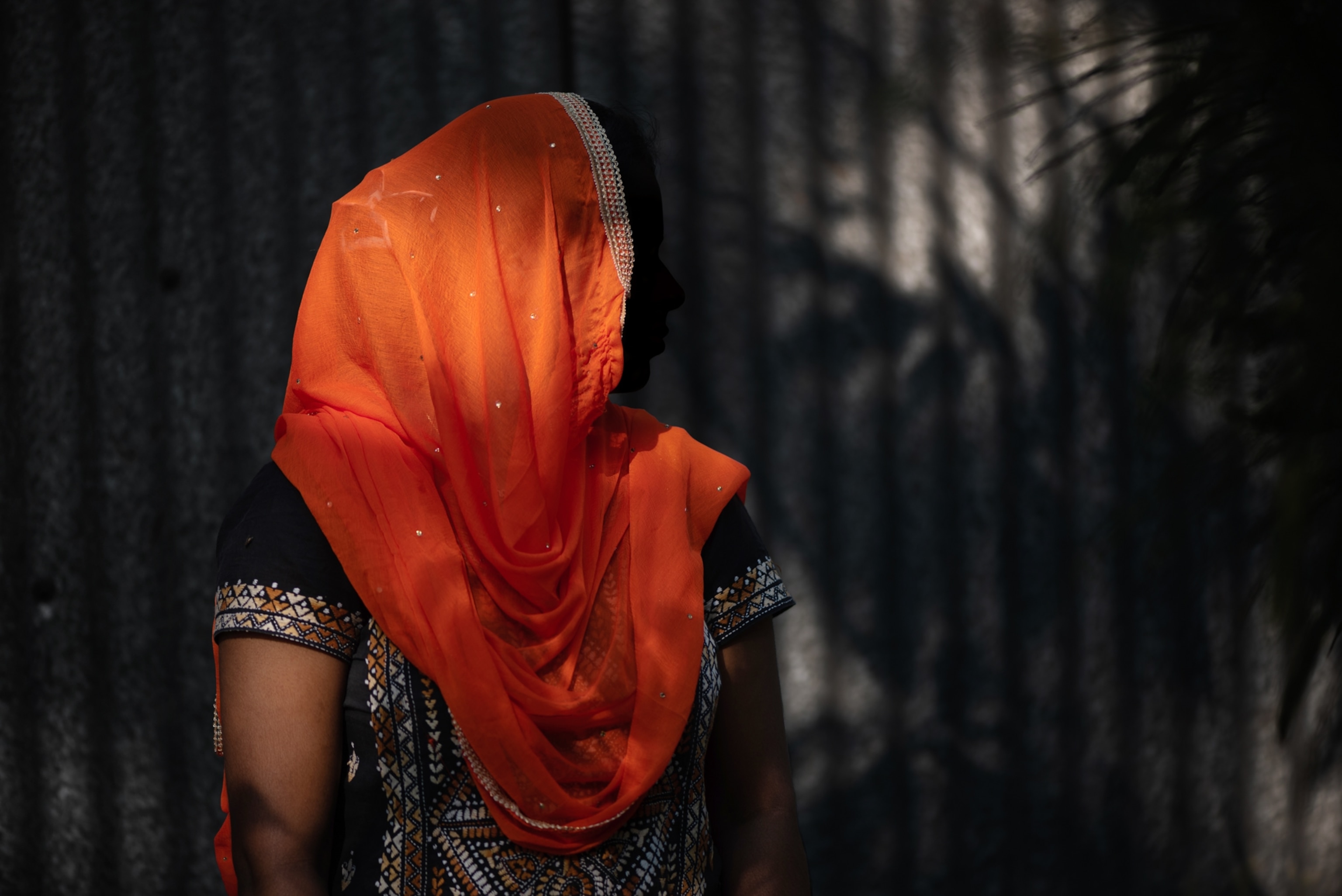 a girl who's orange sari is silhouetted against a textured background