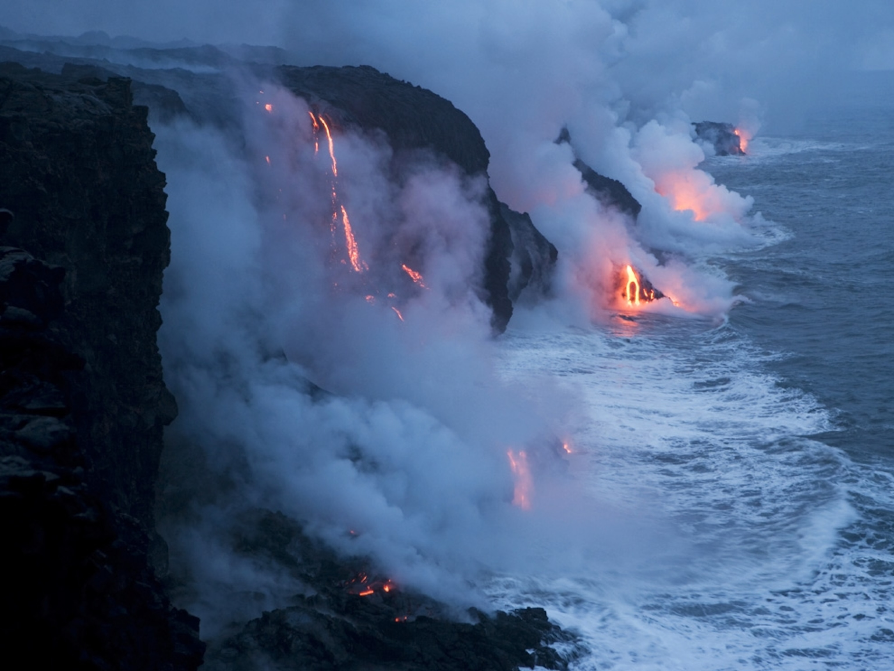 Glowing red lava flows into the ocean