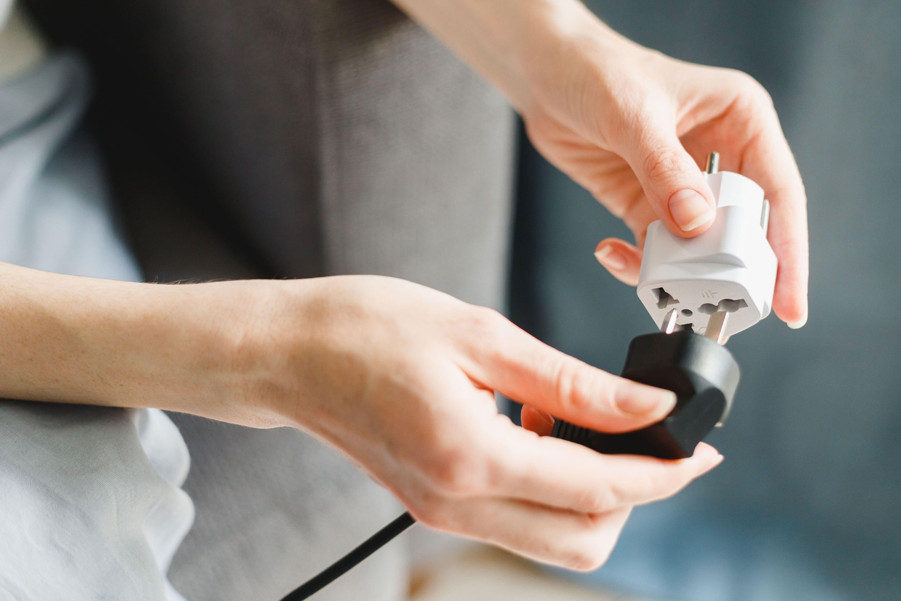 A persons hands plug a black cord into a white adapter.