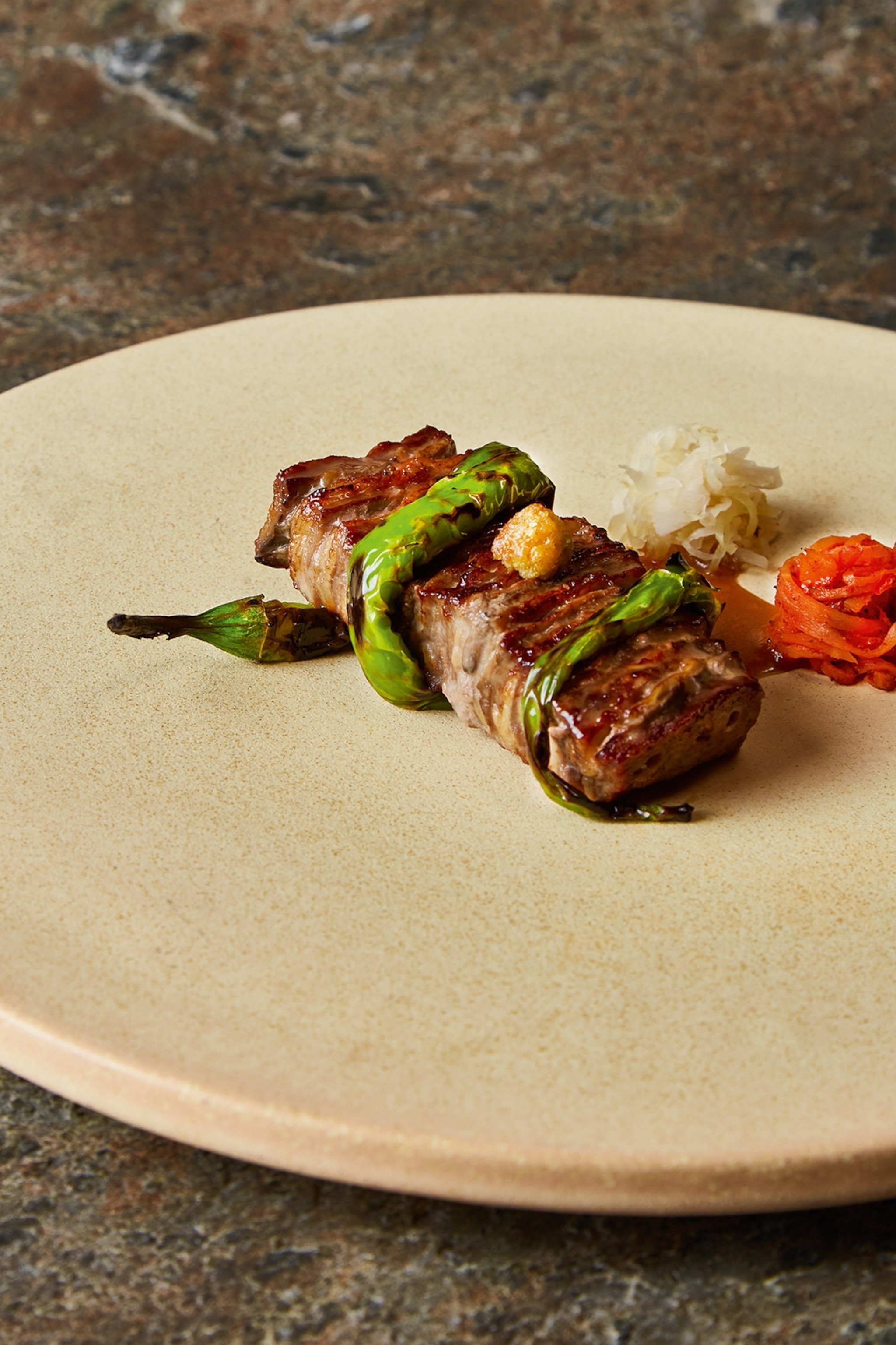 A plate of grilled lamb with a charred, green chili wrapped around it like a snake.