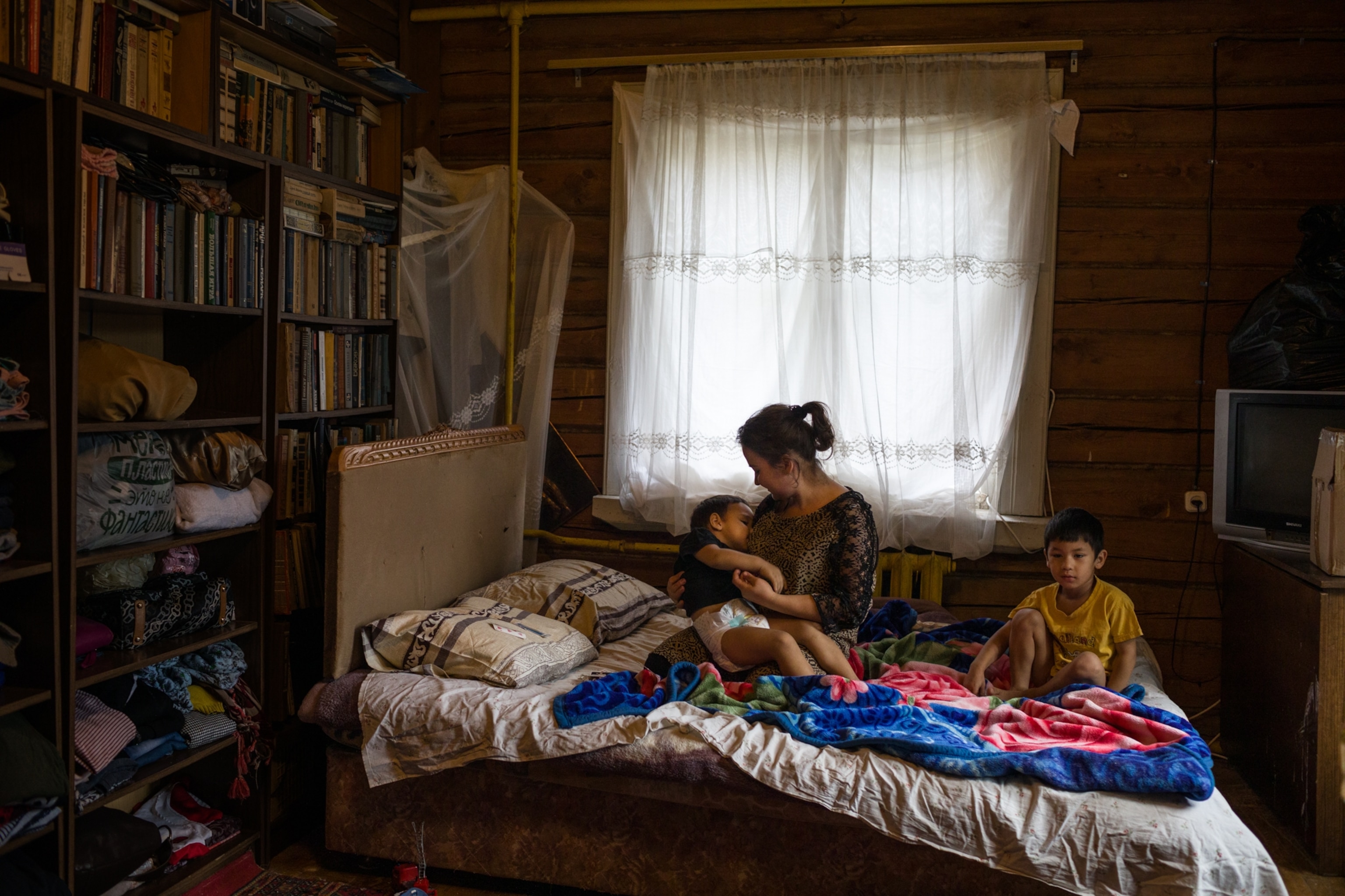 a woman on a bed carrying a child while another child sits on the end of the bed