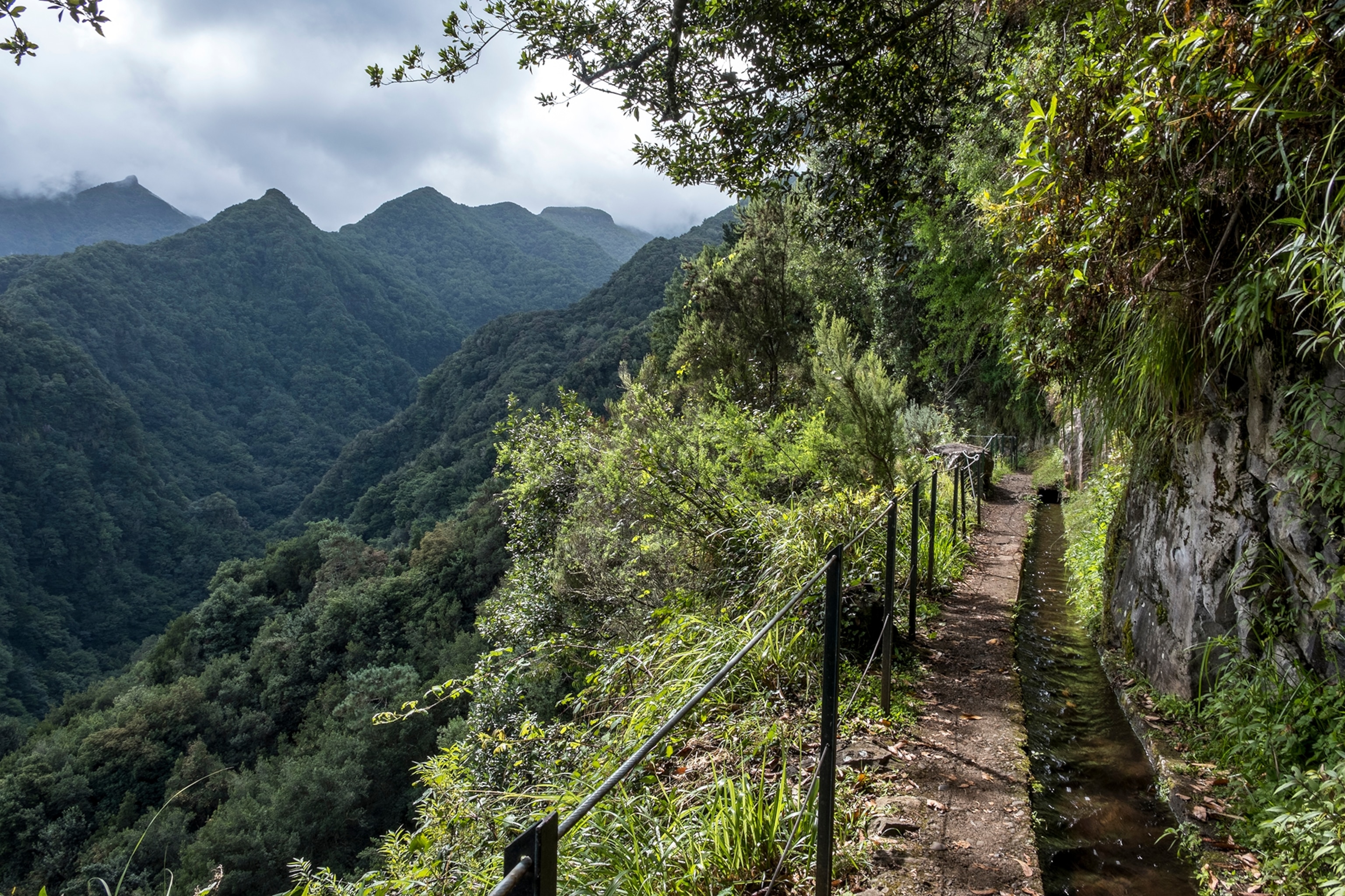 Hiking path along a cliff, mountain range in the background.