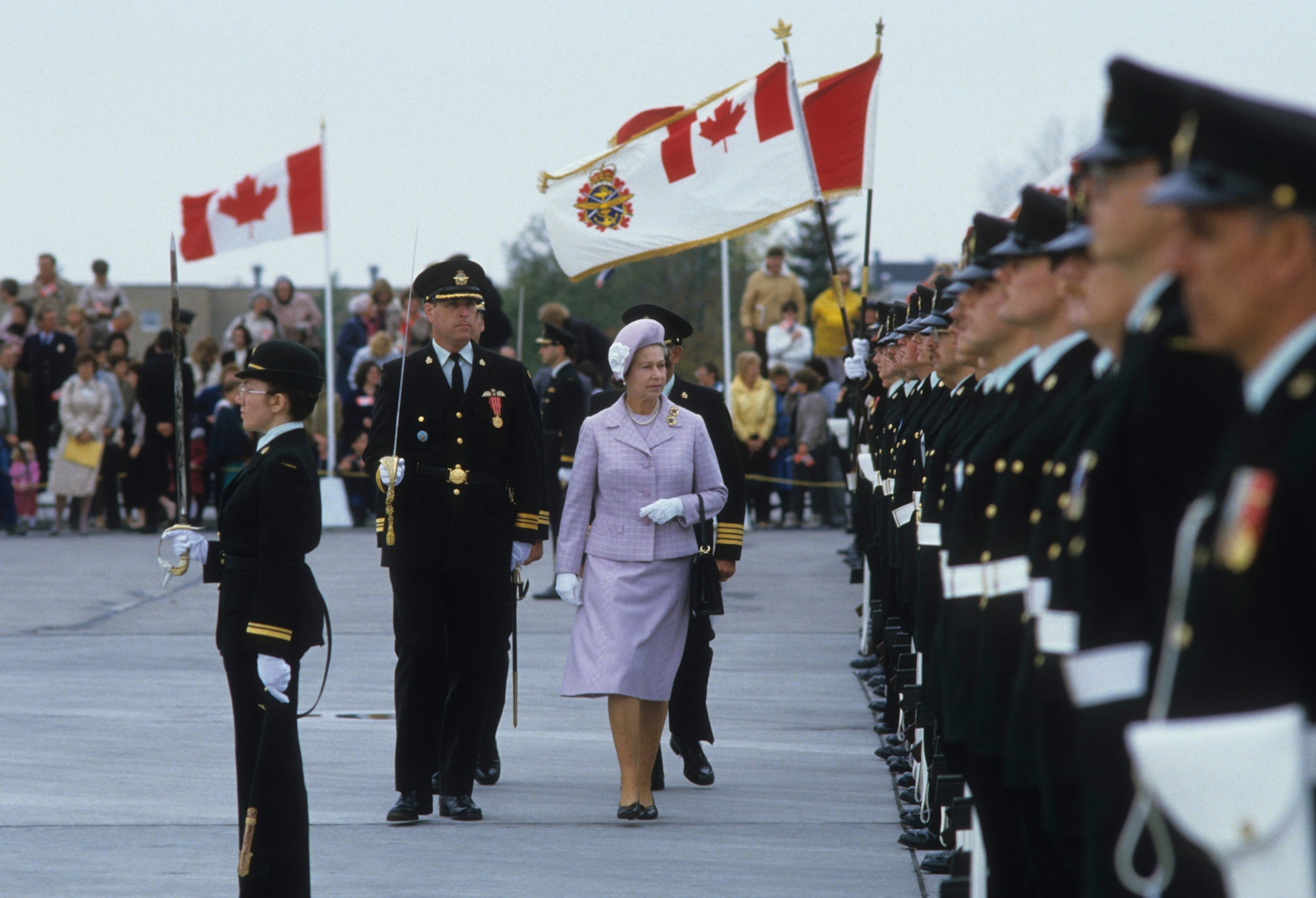 Photo of Queen Elizabeth II walking with soldiers and Canadian flags flying