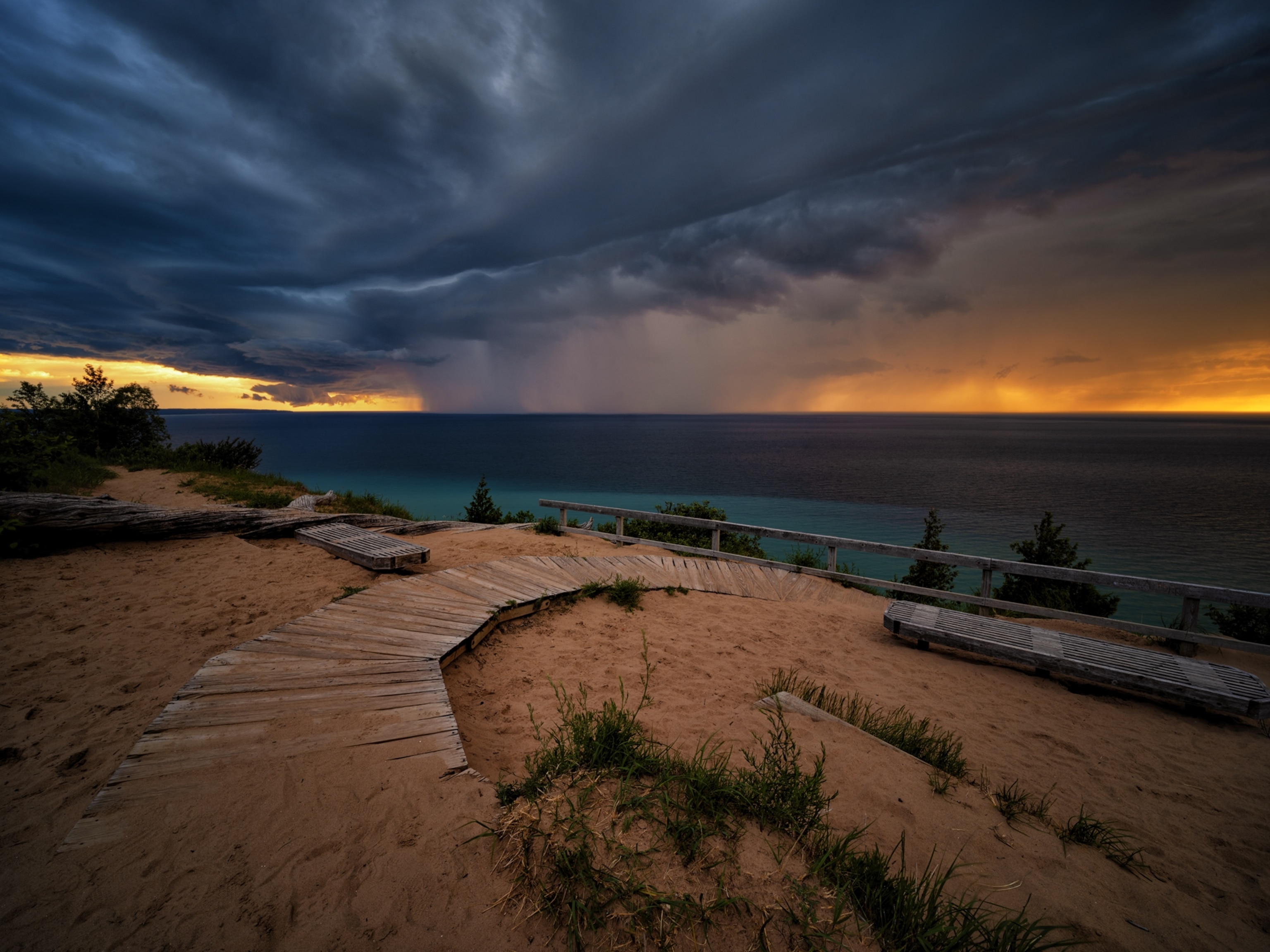 boardwalk over sand by the lake under stormy skies.