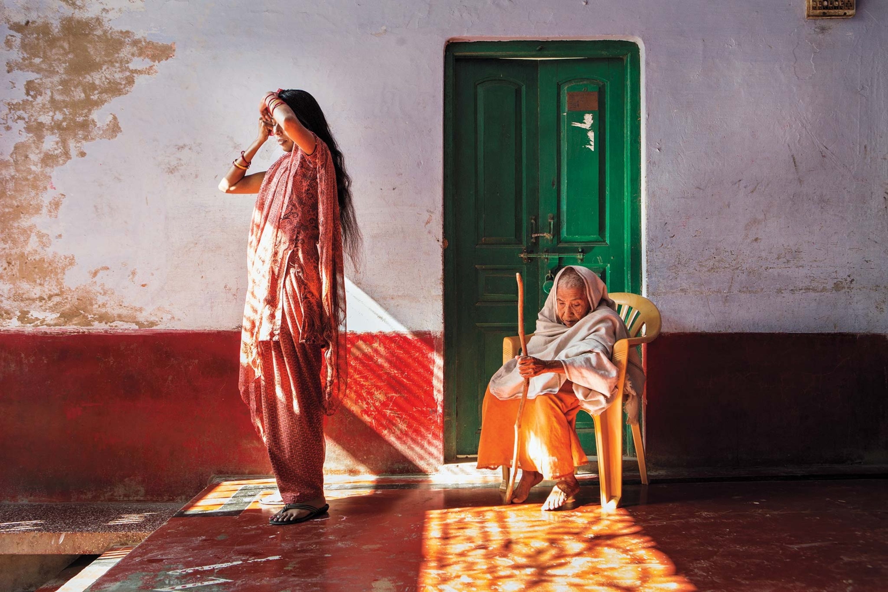 A woman standing and a woman sitting by a green door are widows in a shelter